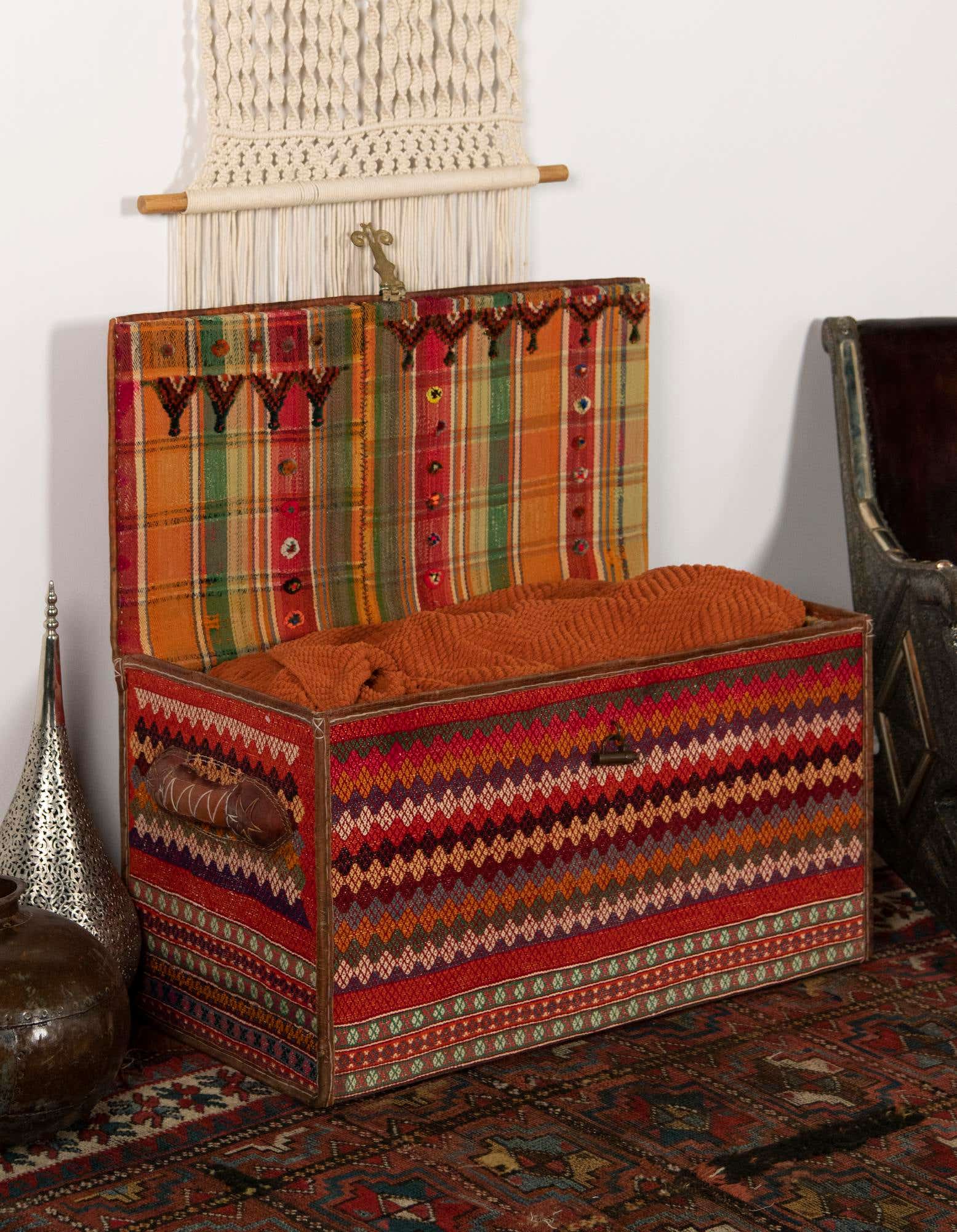 A rectangular 2x3 orange, red, and green traditional rug with intricate patterns, placed under a decorative trunk.