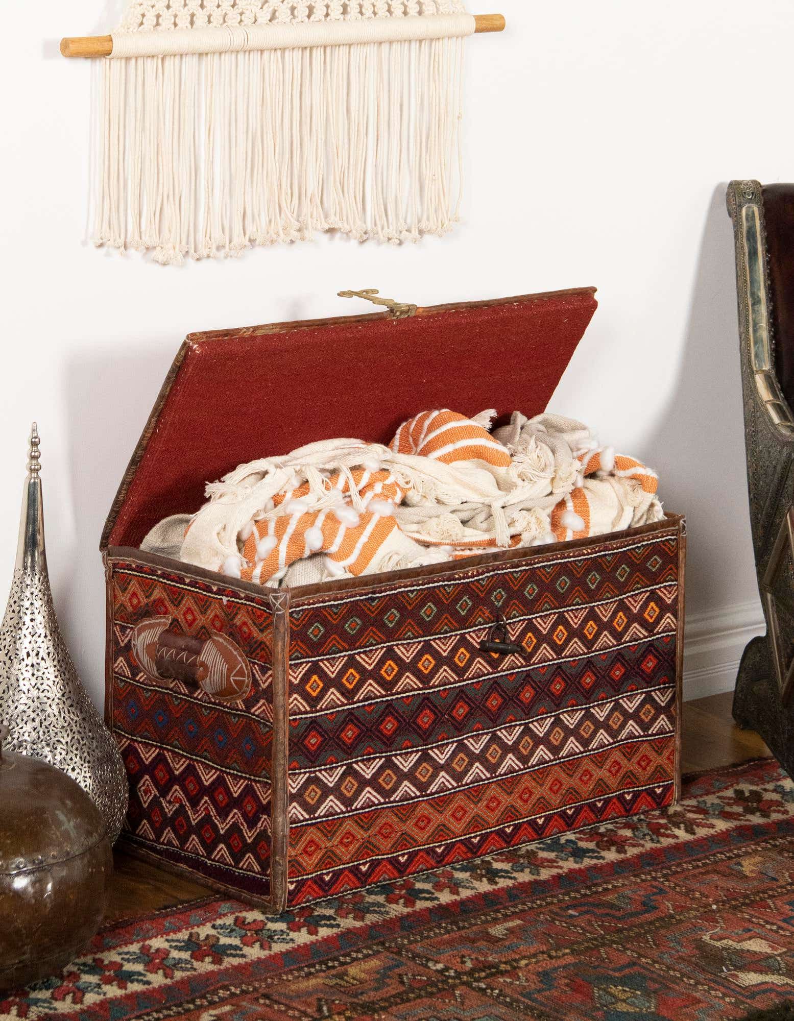 A 1x3 rectangular traditional orange and red rug with an oriental pattern, partially visible under a decorative storage chest.