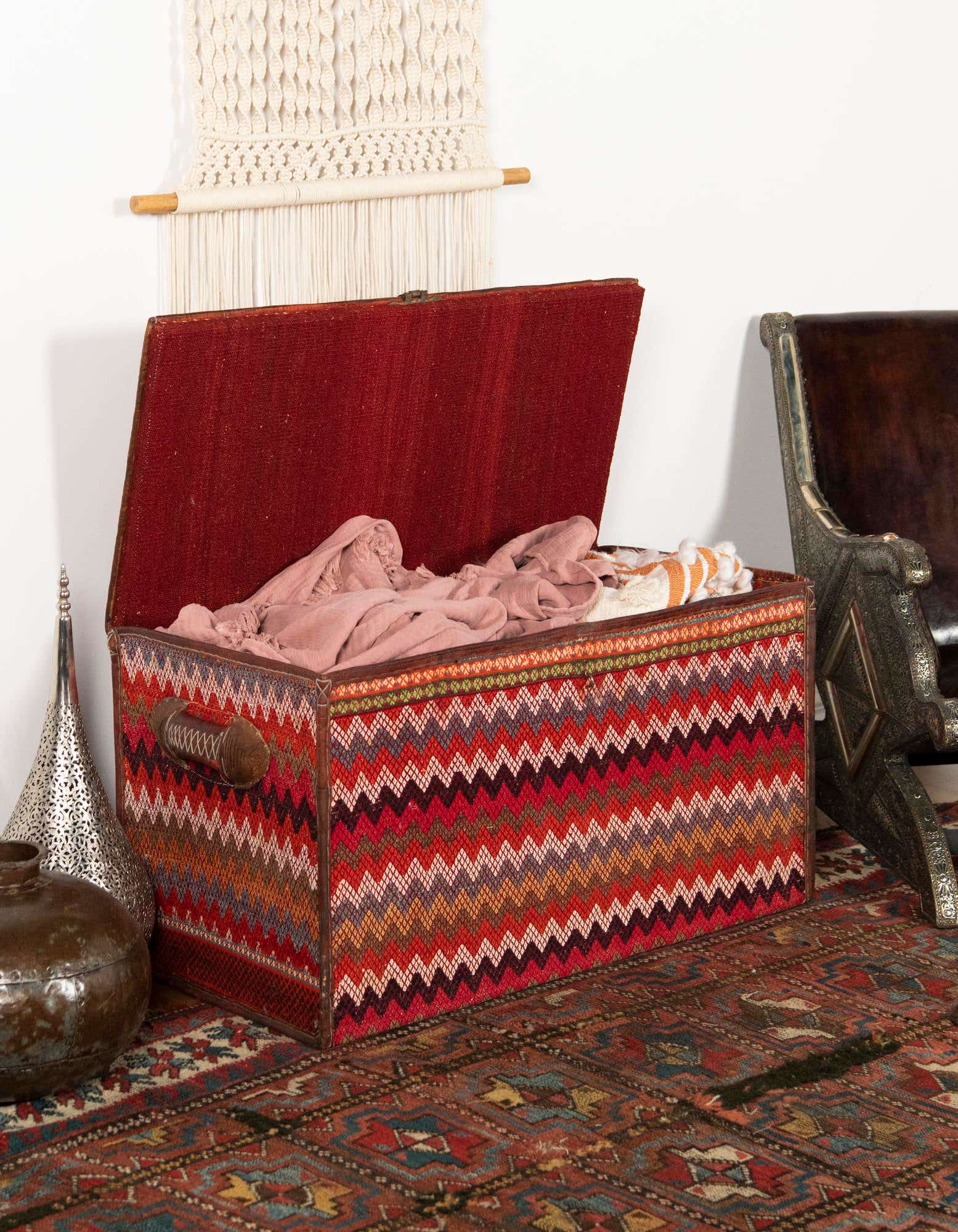 A 2x3 rectangular orange and red Oriental rug with an abstract pattern, grounding a decorative storage trunk in an indoor setting.