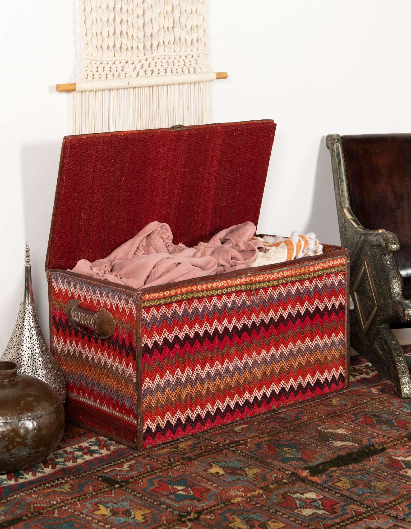 A 2x3 rectangular orange and red Oriental rug with an abstract pattern, grounding a decorative storage trunk in an indoor setting.