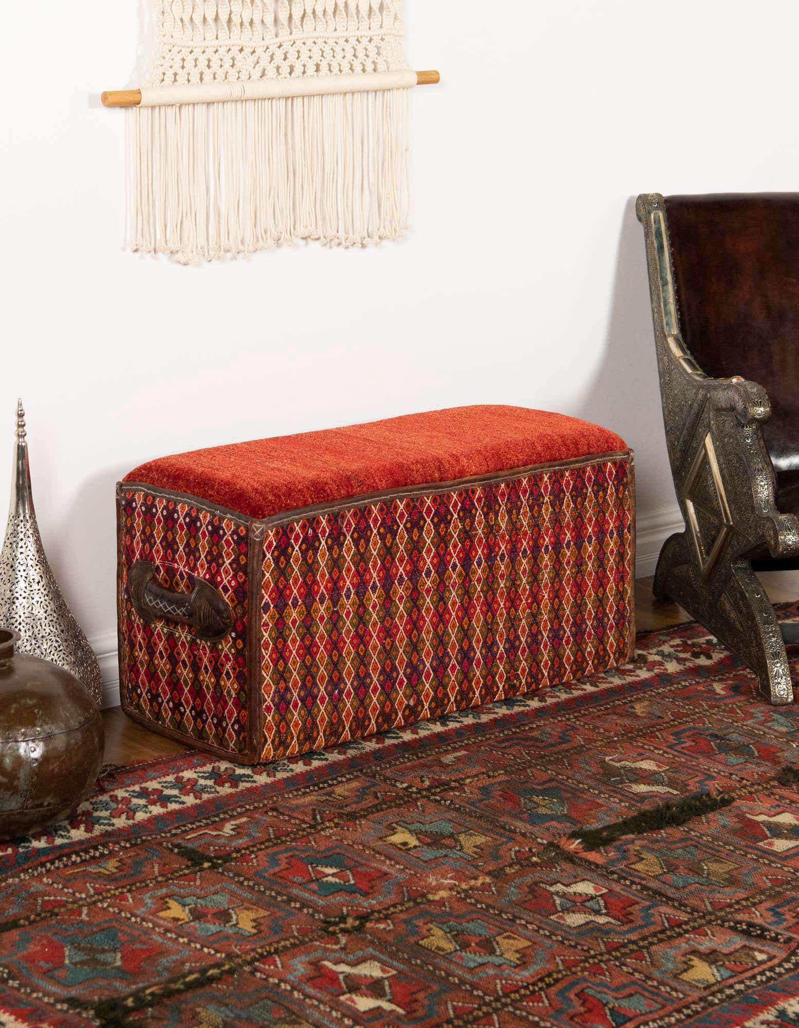 A 2x3 rectangular traditional rug in shades of orange and red with an intricate oriental pattern, placed under a patterned storage ottoman.