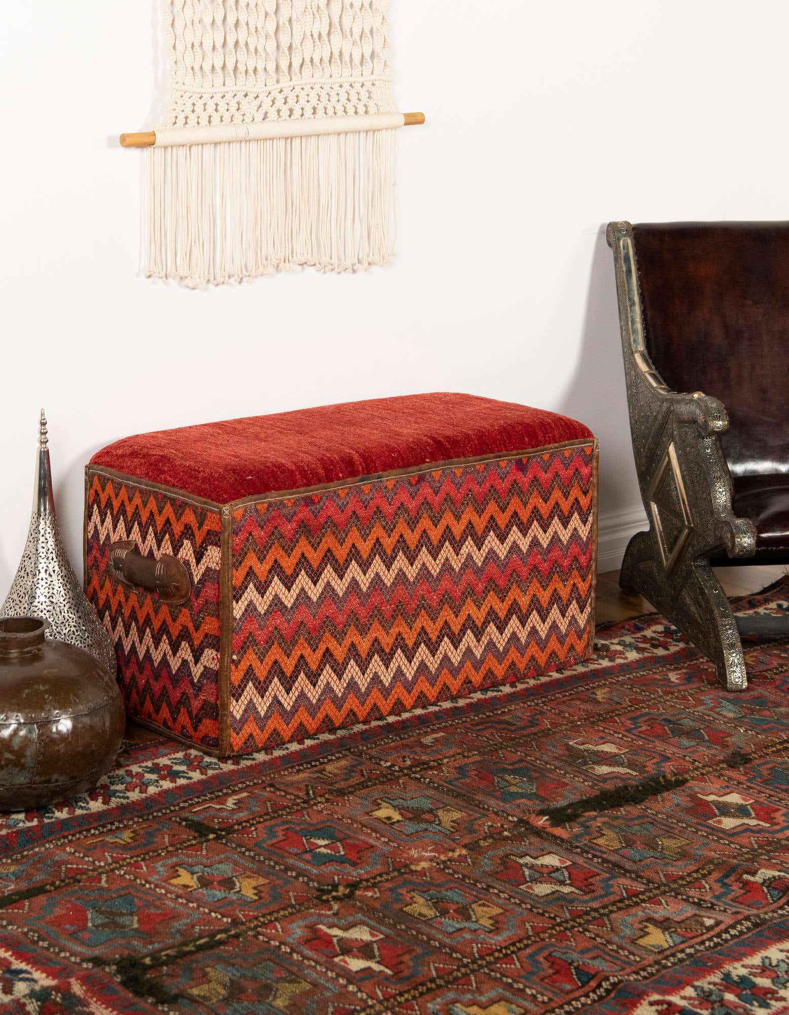 A 2x3 rectangular rug with a traditional Oriental pattern in shades of orange, red, and blue, under a patterned storage bench.