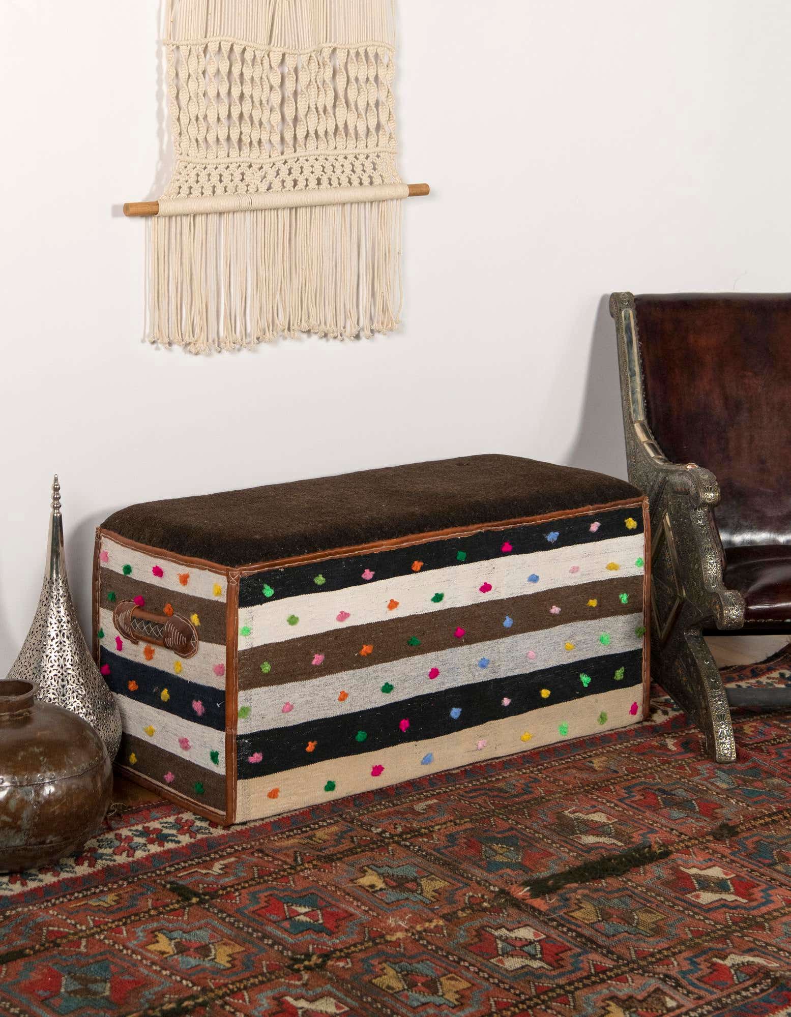 A rectangular 2x3 brown, tan, and black striped rug with colorful polka dots, under a brown upholstered bench in a living room.