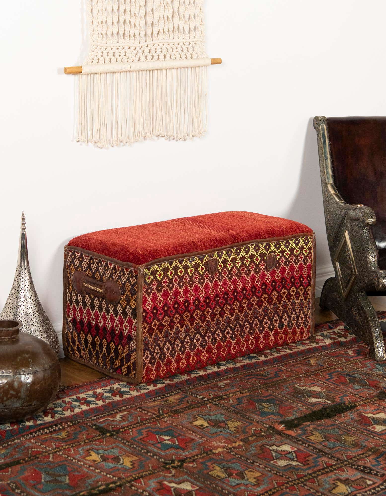 A 2x3 rectangular orange and red traditional rug with intricate patterns, placed under a patterned ottoman in a living room.