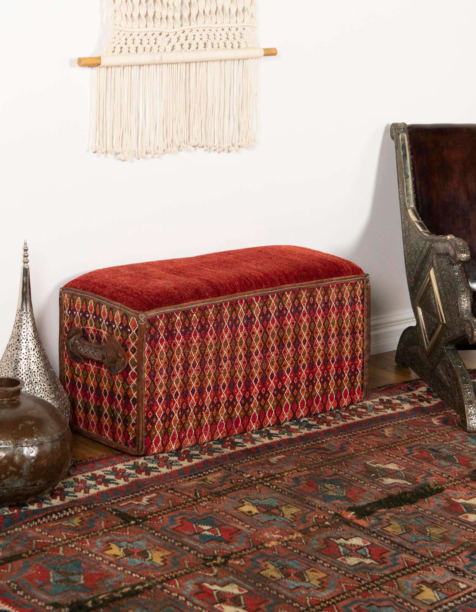 A 2x3 rectangular orange and red traditional rug with intricate patterns, under a patterned ottoman in a living room setting.