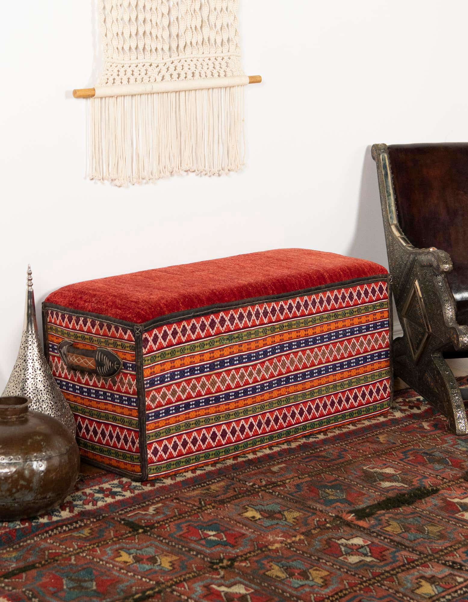 A 2x3 rectangular Oriental rug in oranges and reds with intricate patterns, placed under a patterned ottoman.