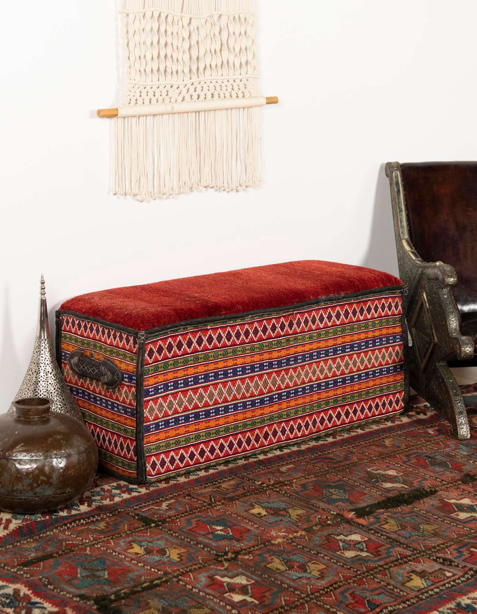 A 2x3 rectangular rug with a distressed modern abstract pattern in shades of orange, red, and blue, under a colorful patterned ottoman.