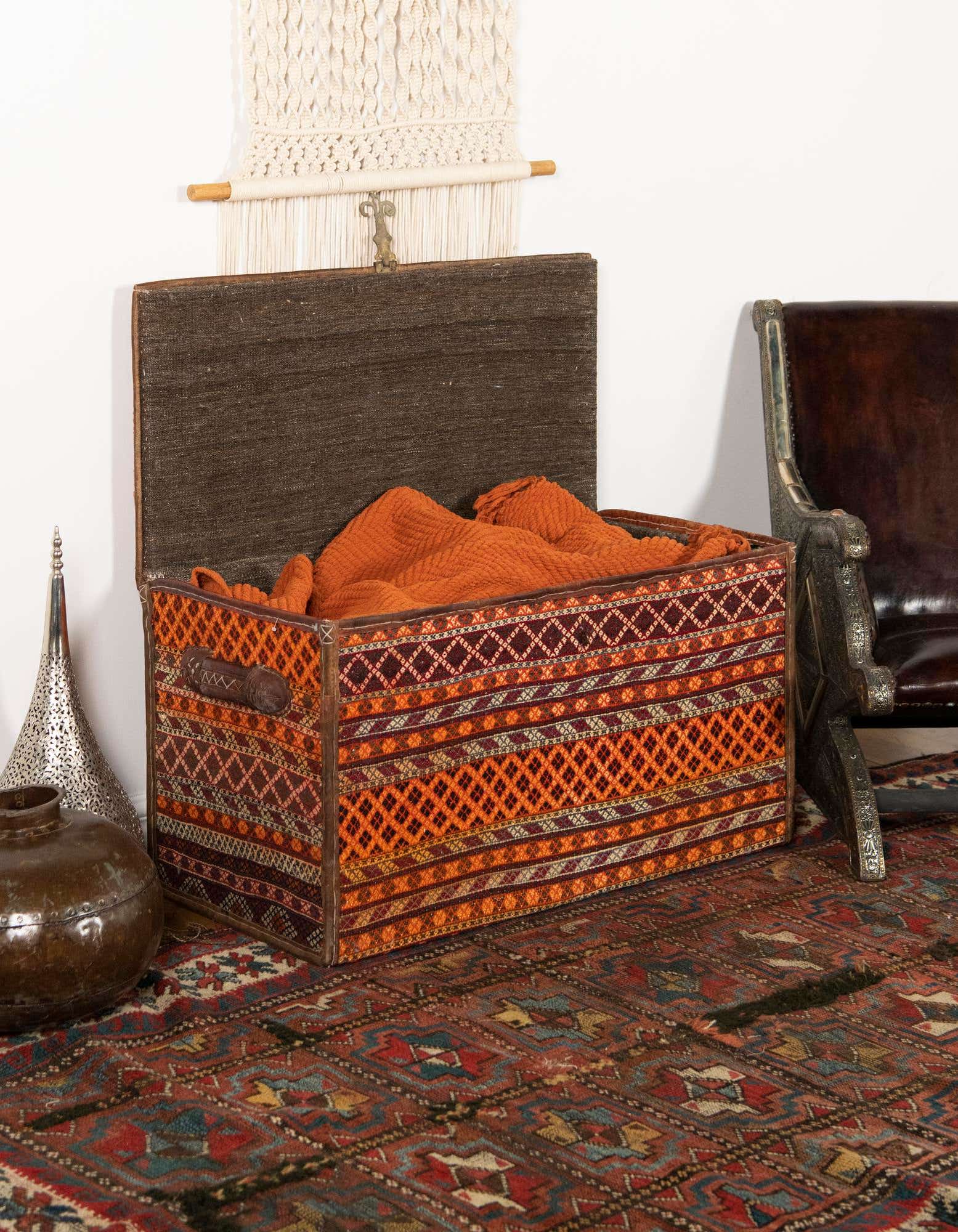 A 2x3 rectangular rug with a modern abstract pattern in shades of orange and red, complementing a decorative storage chest in a cozy indoor setting.