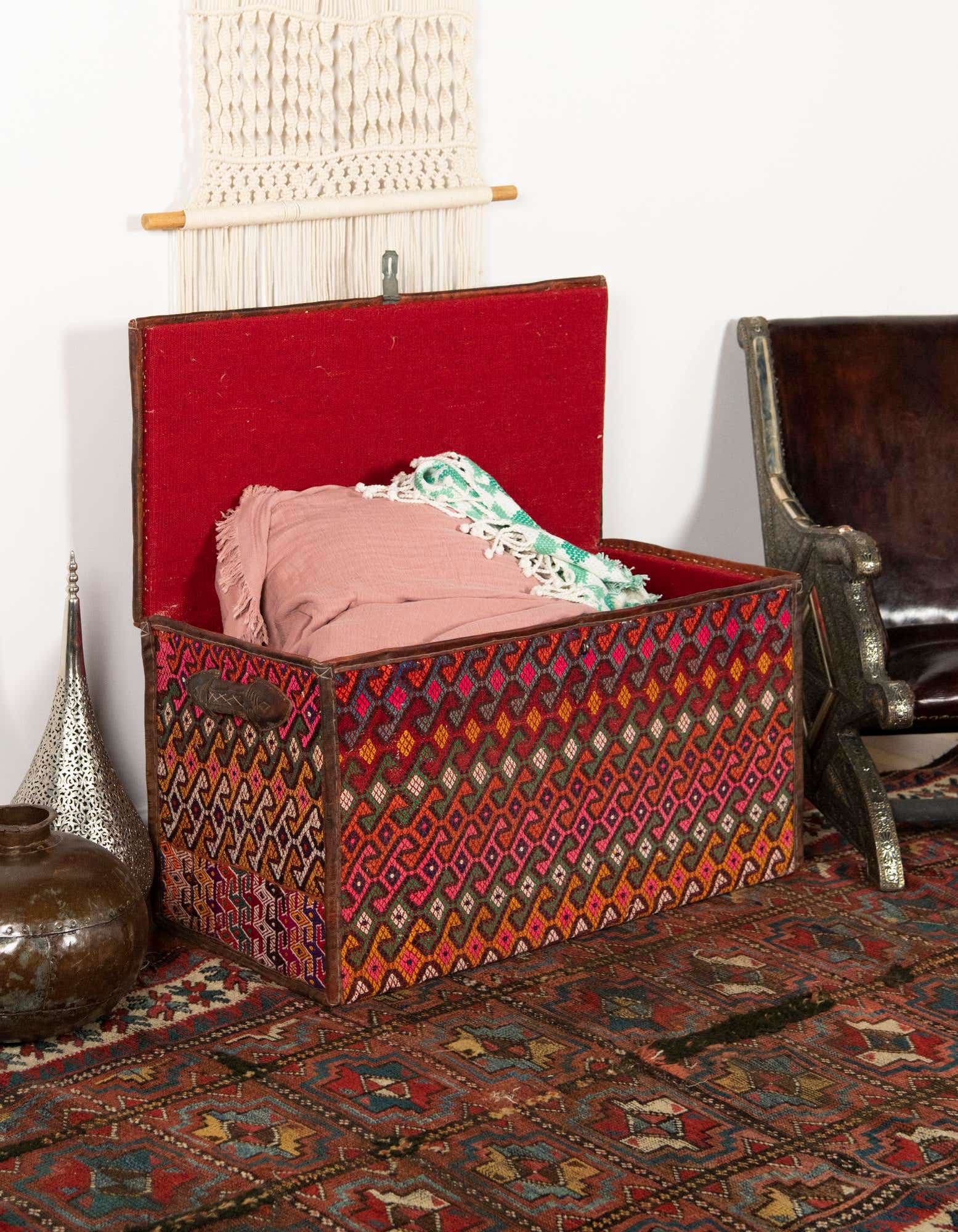 A 2x3 rectangular rug with a distressed orange and red abstract pattern, grounding a decorative storage chest.
