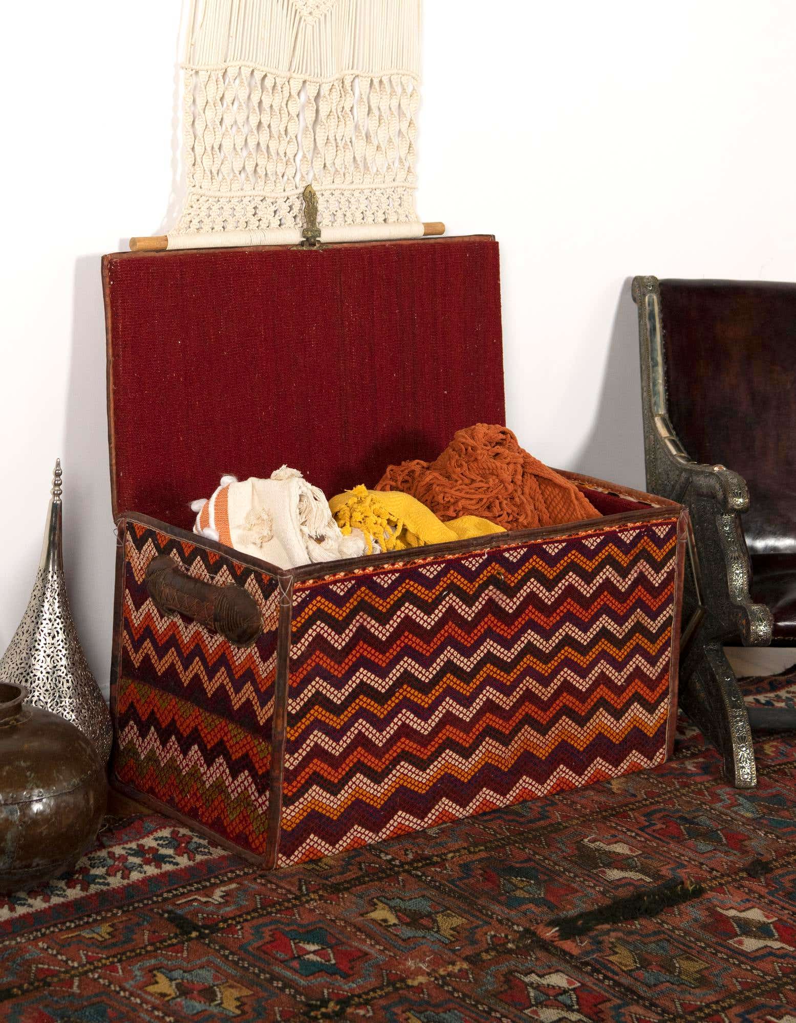 A 2x3 rectangular rug with a distressed, intricate geometric pattern in shades of red, orange, and blue, under a decorative storage trunk.