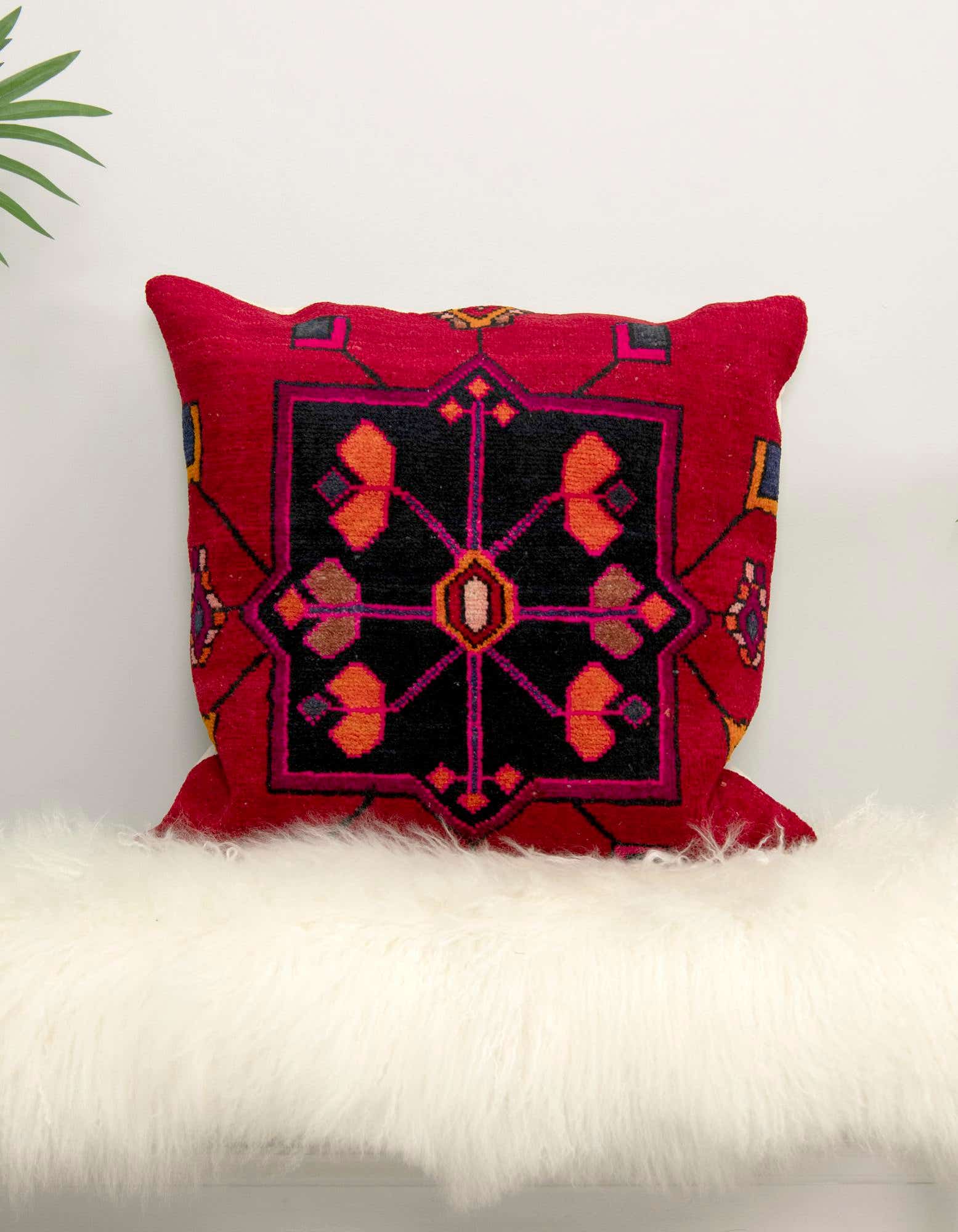 A vibrant red 25 Euro rectangular pillow with a black, orange, and pink Persian pattern, resting on a fluffy white rug.