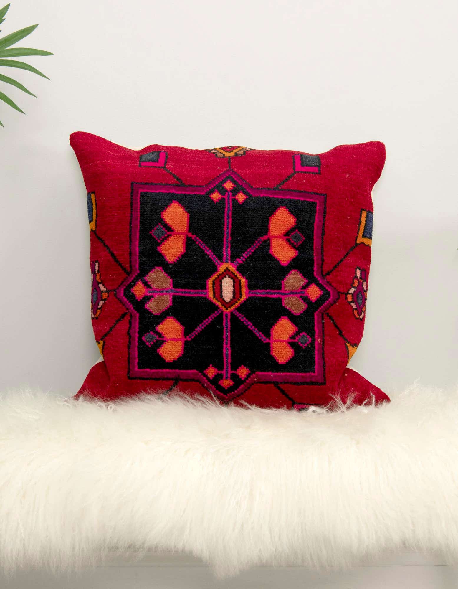 A vibrant red 25 Euro rectangular pillow with a black, orange, and pink Persian pattern, resting on a fluffy white rug.