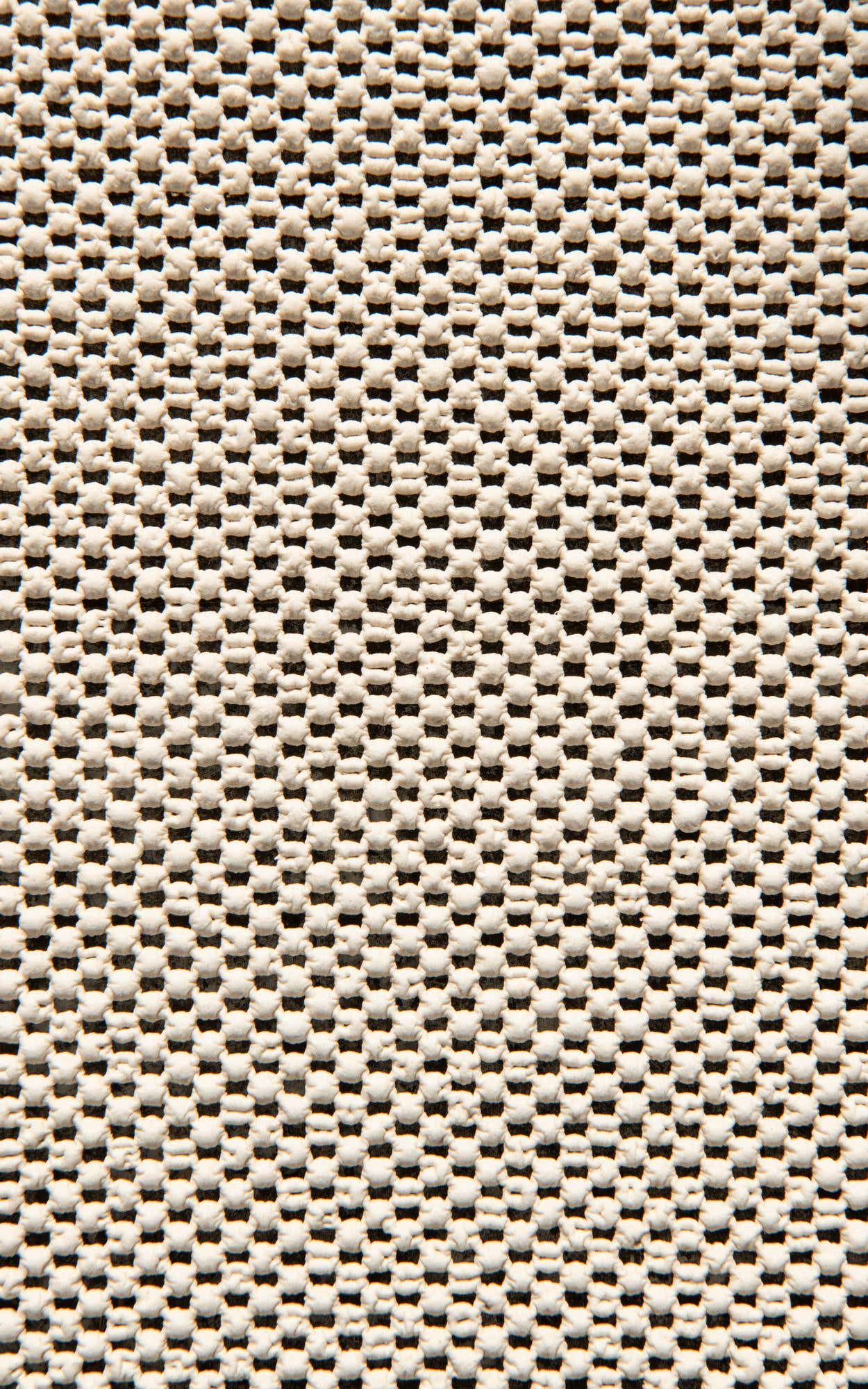 Close-up of a white, textured rug pad with a grid pattern of small, raised nubs designed to prevent slipping.