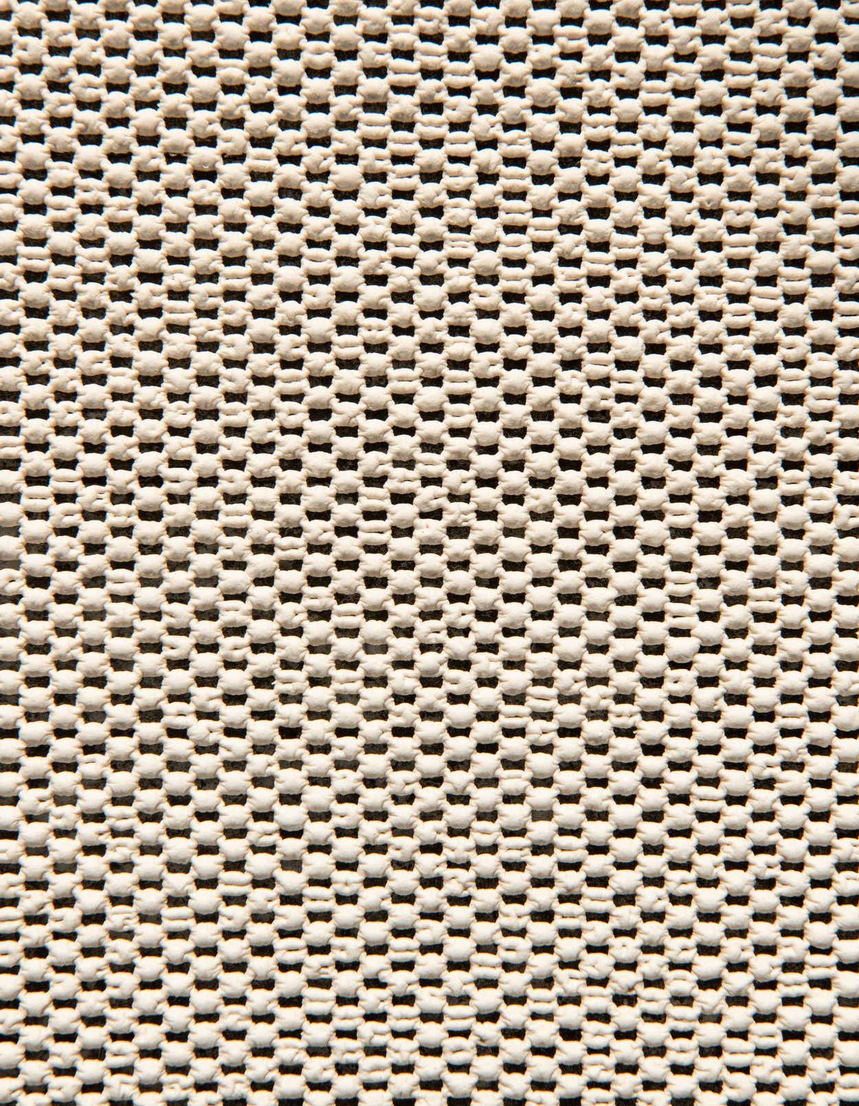 Close-up of a rectangular rug pad with a grid pattern of raised, textured white squares on a dark gray backing.