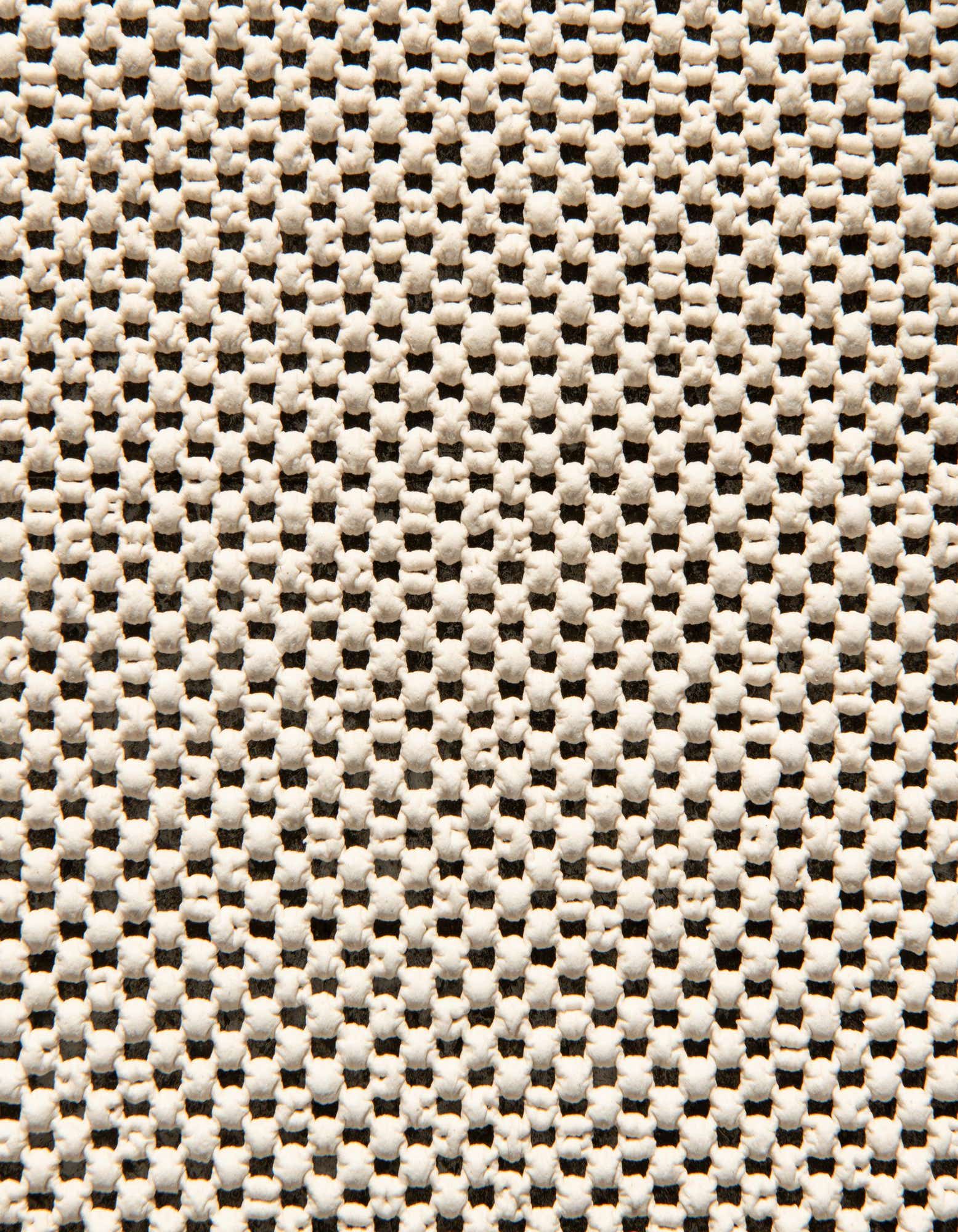 Close-up of a white, textured rug pad with a grid pattern of small, raised rubber dots for non-slip grip.