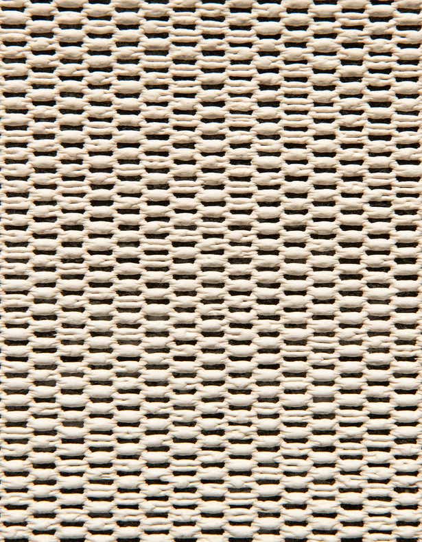 Close-up of a textured rug pad with a grid pattern of raised beige nodes on a dark background, providing non-slip grip.