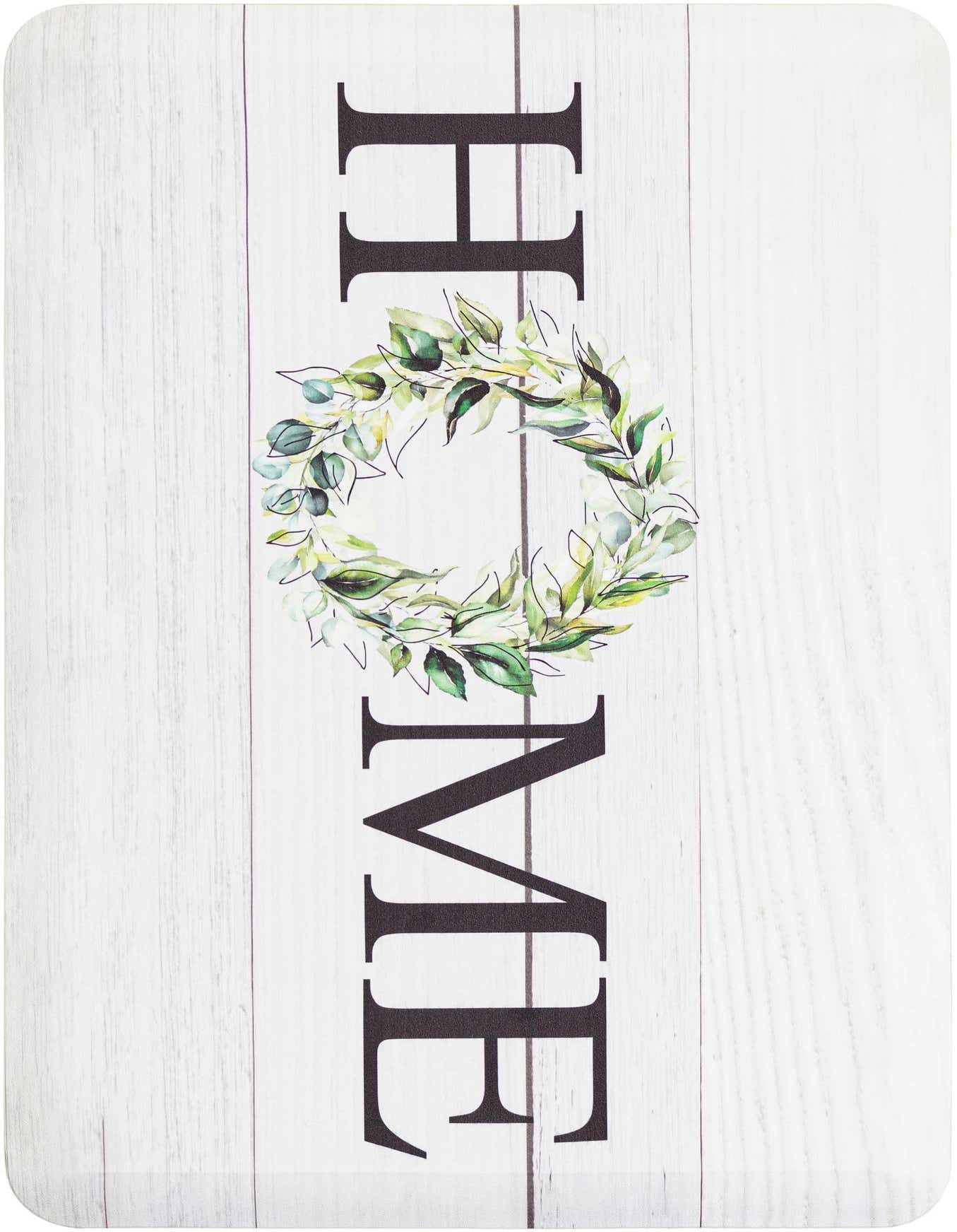 A 2x3 rectangular comfort mat with a white wood plank background. Black letters spell 'HOME' vertically, with a green leafy wreath replacing the 'O'.