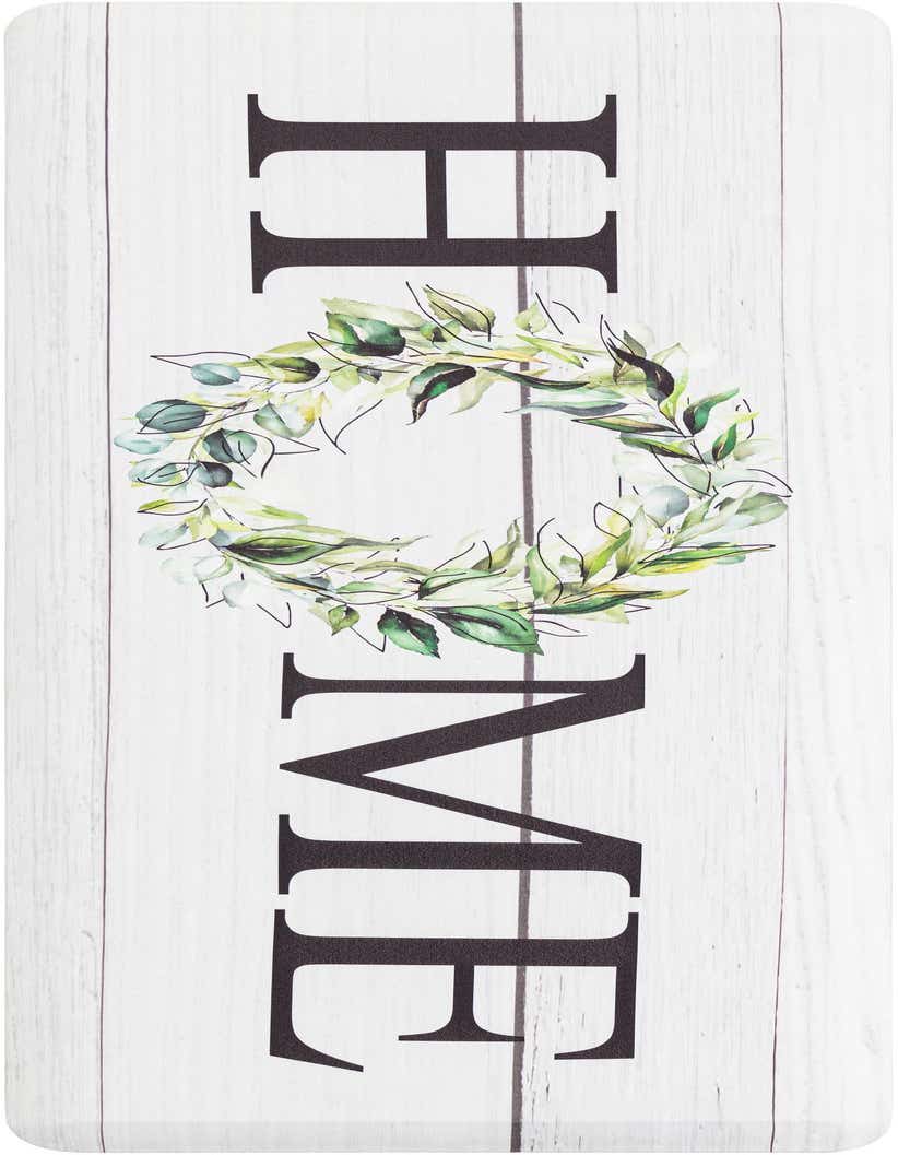 A 2x5 rectangular white comfort mat with a rustic wood plank design and 'HOME' in black letters, featuring a green leaf wreath for the 'O'.