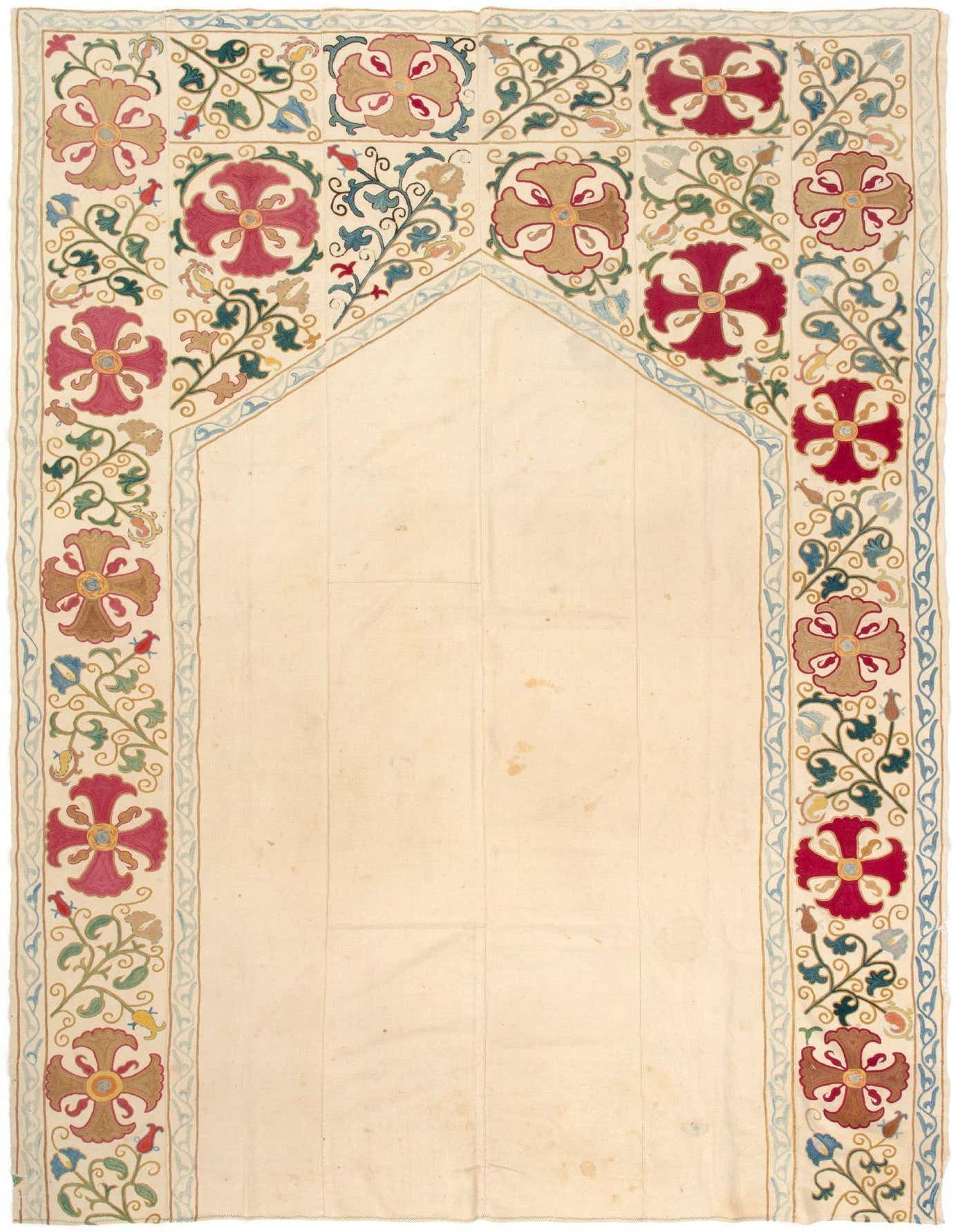 A 5x8 rectangular Suzani rug with an ivory field and a border of intricate floral embroidery in red, brown, blue, and green.