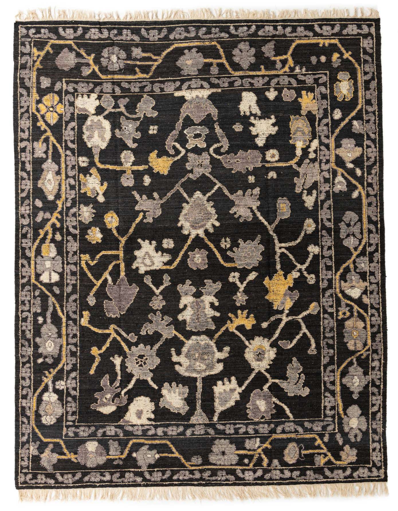 A 9x12 rectangular black wool rug with a modern floral pattern in grey, cream, and gold, featuring a border and fringe.