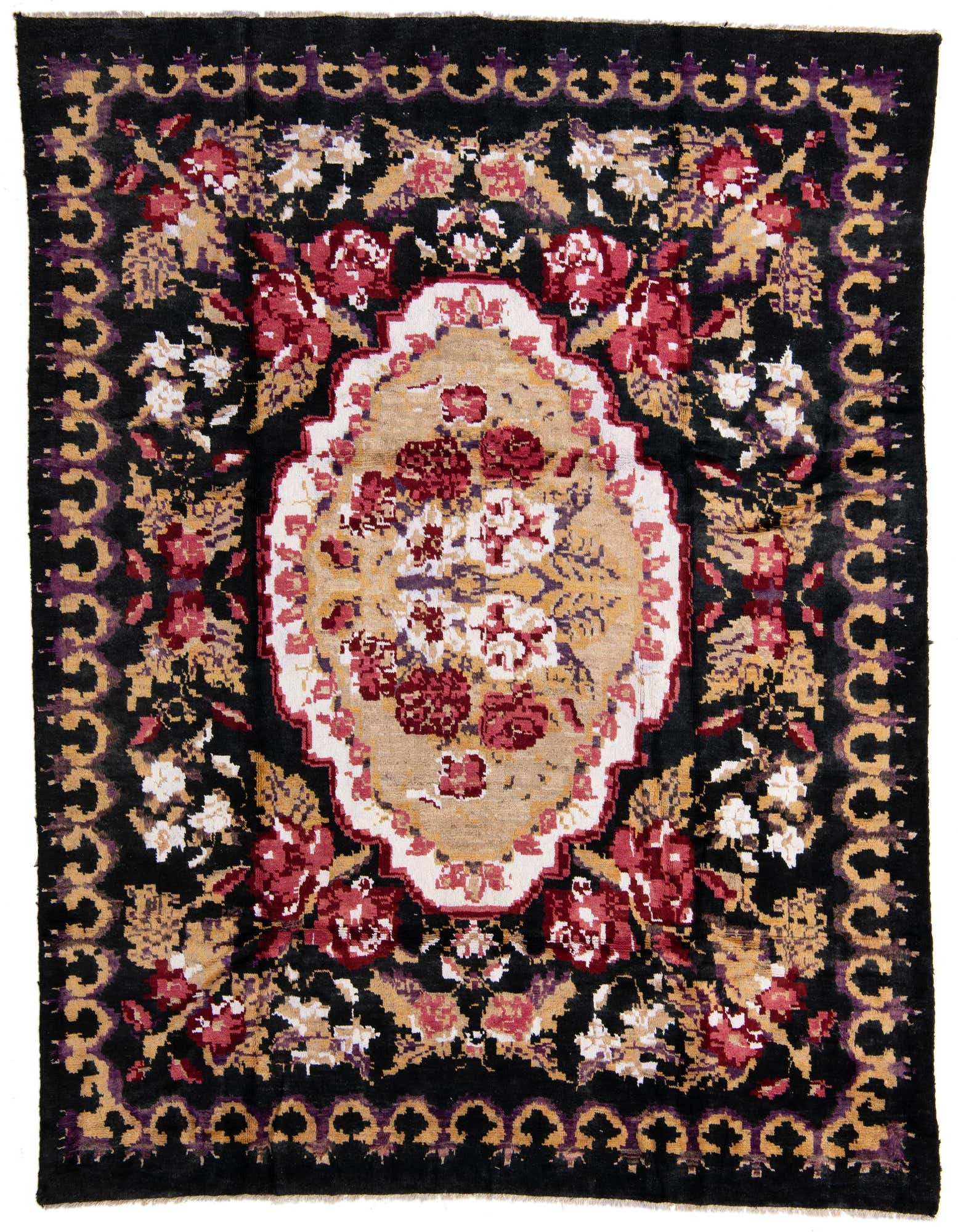8x10 rectangular black wool shag rug with a central beige medallion and red, white, and purple floral patterns.