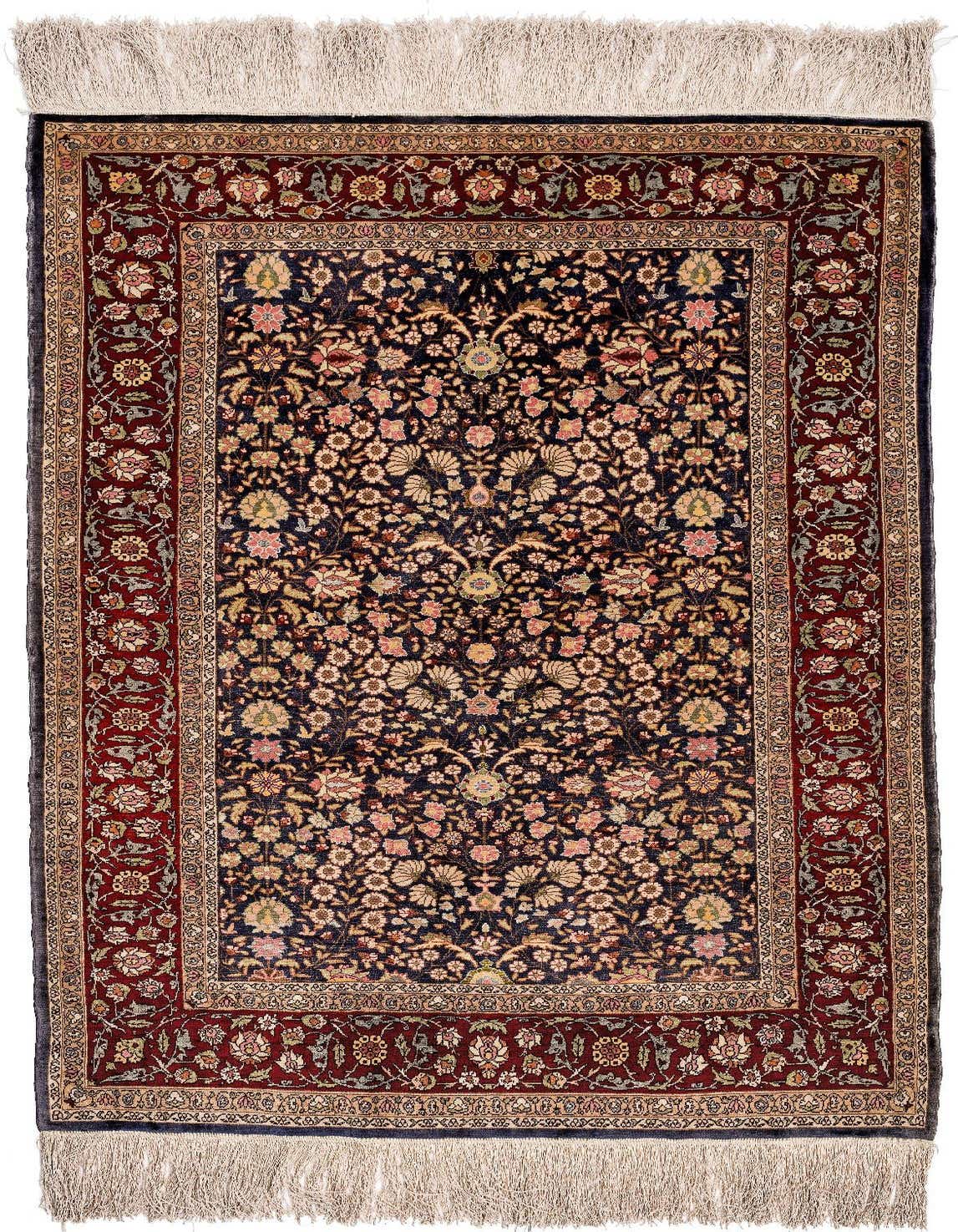 A 2x3 rectangular handmade indoor rug with a dark blue field and intricate floral patterns in pink, gold, and green, framed by a deep red border.