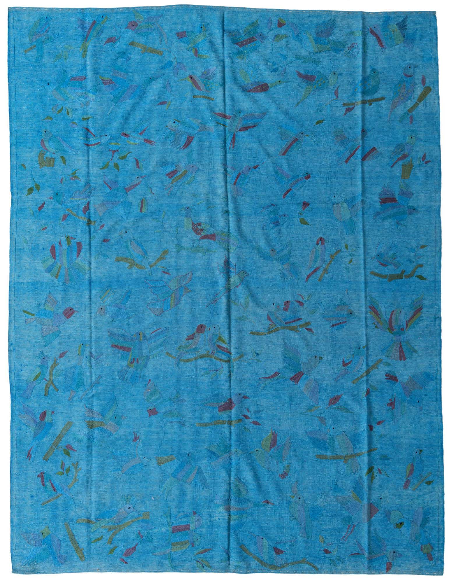 A rectangular 8x11 blue flatweave rug with a scattered pattern of colorful birds and branches.