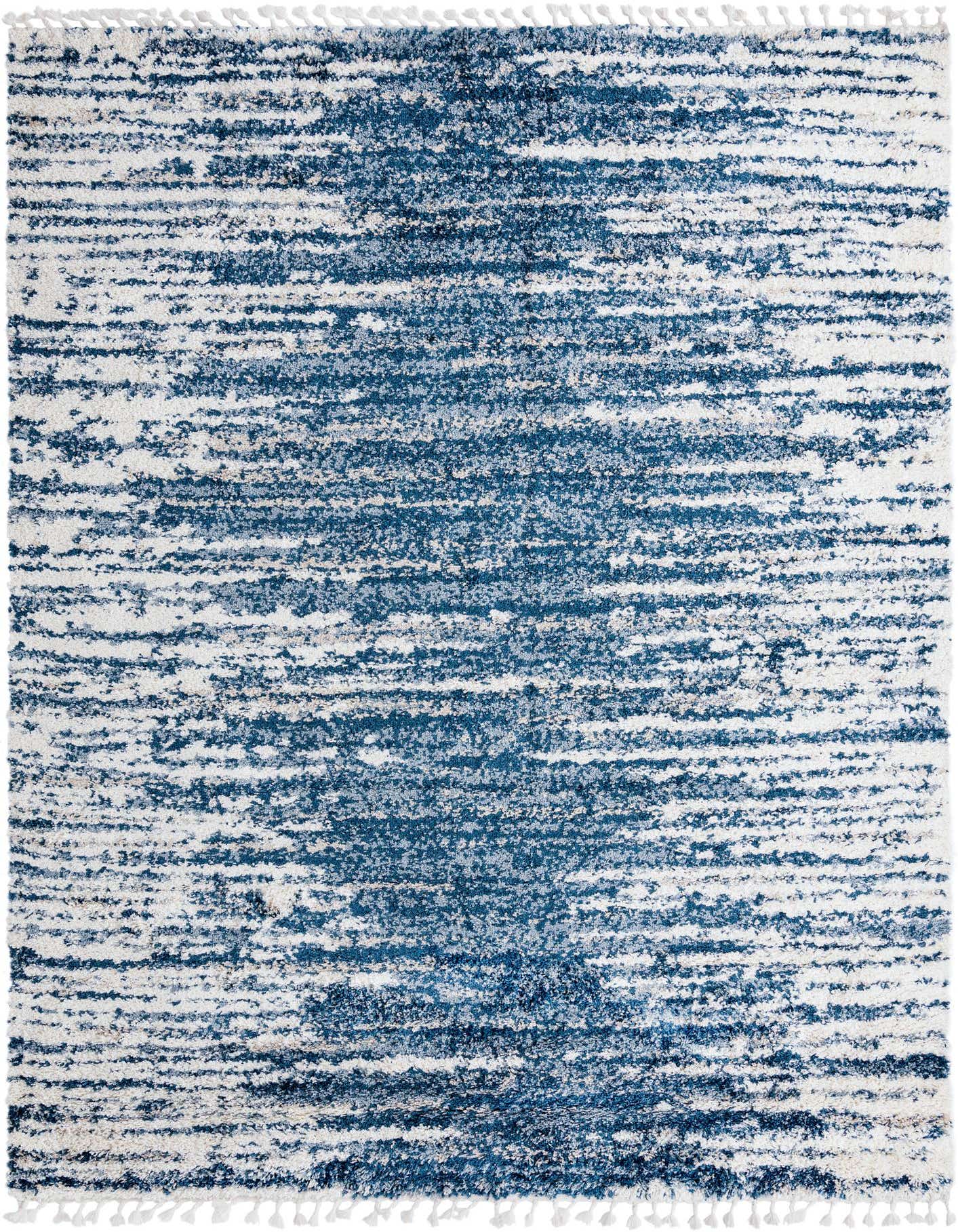 A 9x12 rectangular Serenity Shag rug with an abstract pattern of varying blue tones and white, featuring decorative tassels.