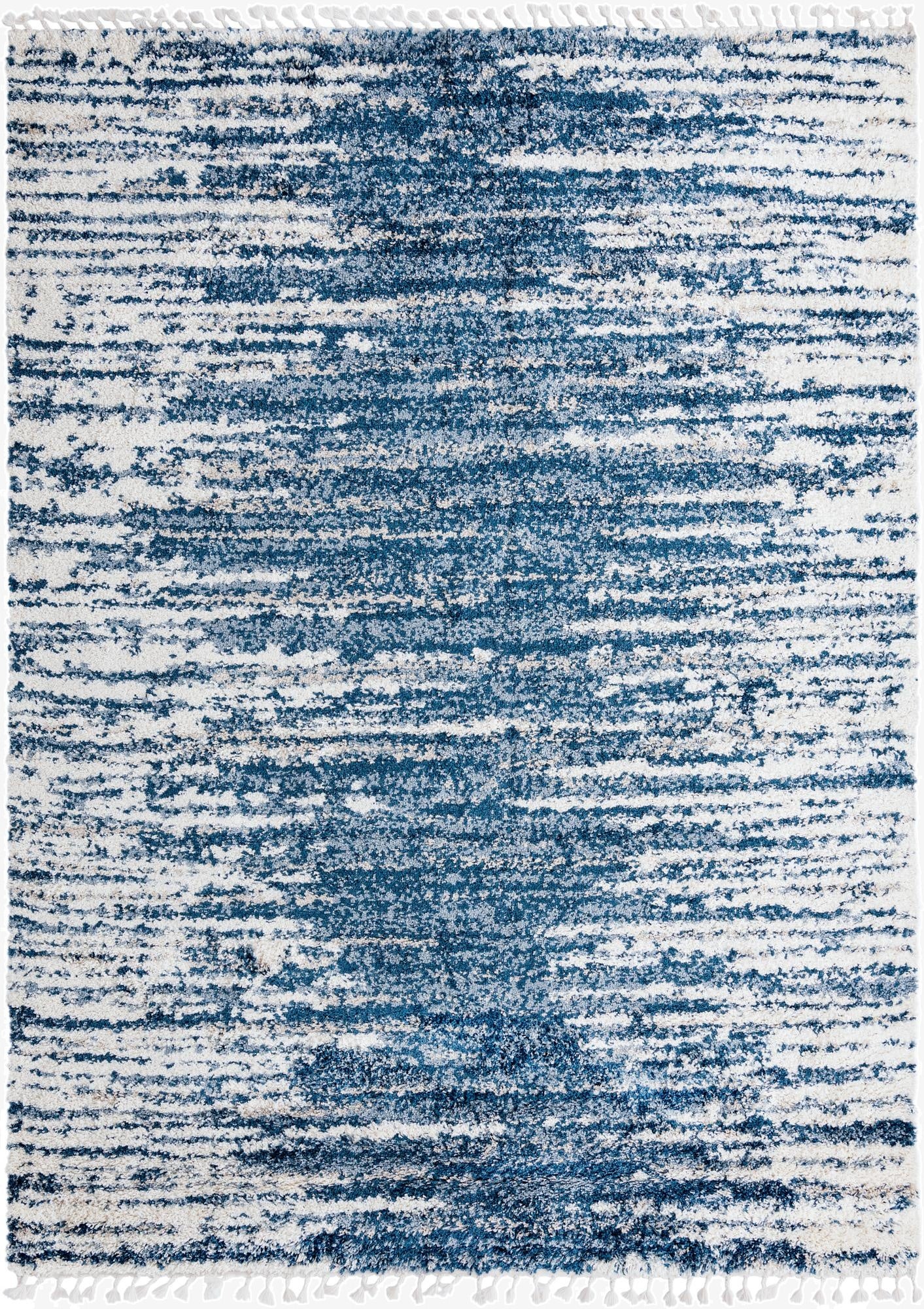 A 9x12 rectangular Serenity Shag rug with an abstract pattern of varying blue tones and white, featuring decorative tassels.
