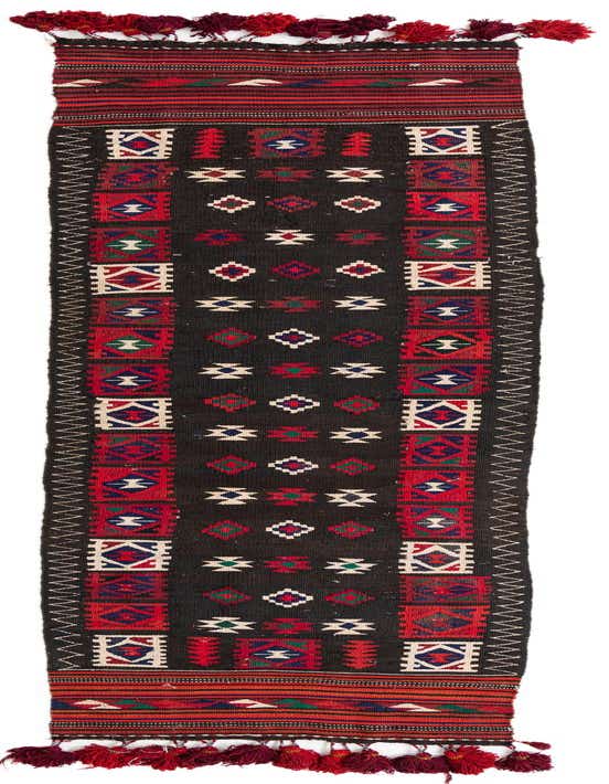 A long, narrow Kilim Fars runner rug with a dark brown background, featuring colorful tribal geometric patterns in red, blue, green, and white, with red tassels at both ends.