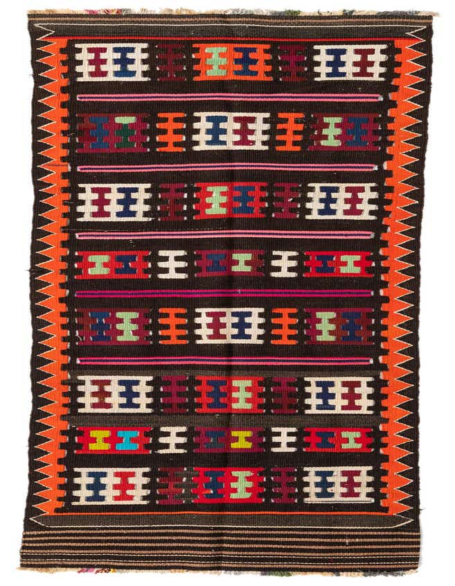 A 10 Ft Kilim Fars runner rug with a dark brown background, featuring colorful tribal geometric patterns in red, orange, green, blue, and white, with orange zigzag borders.