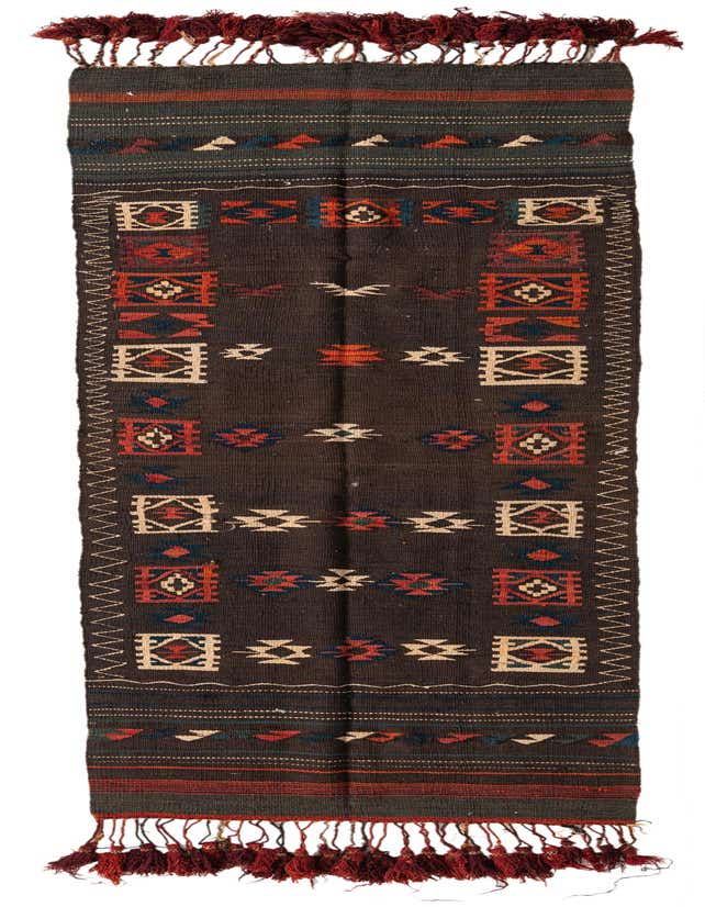 A long, narrow Kilim Fars 11 ft runner rug in shades of brown with tribal patterns in red, blue, and cream, featuring decorative tassels.