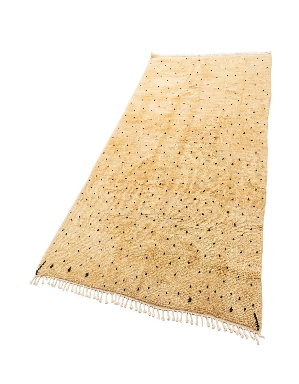 A rectangular 6x9 ivory wool rug with a medium pile and scattered black polka dots, featuring fringed edges.