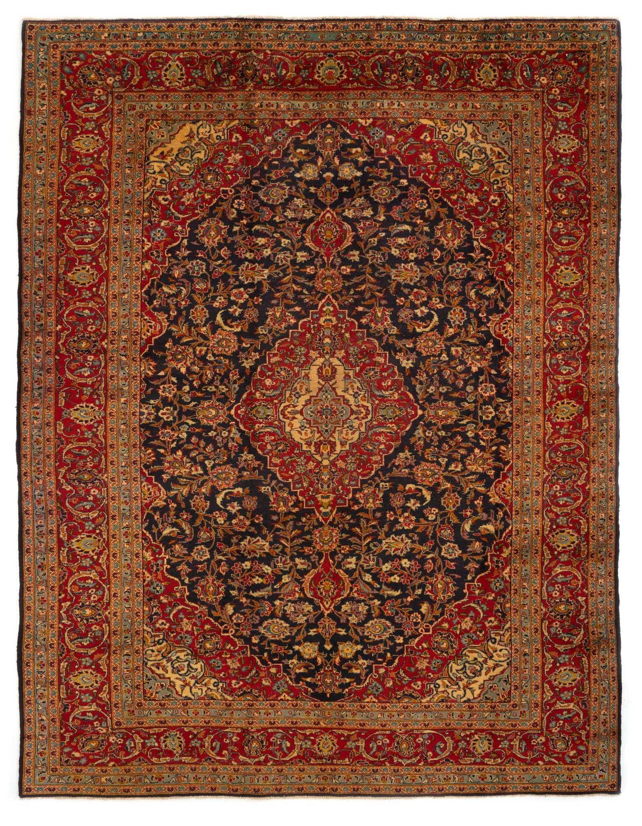A large 9x12 rectangular Kashan Persian rug with a dark blue field and intricate red, gold, and blue floral patterns.