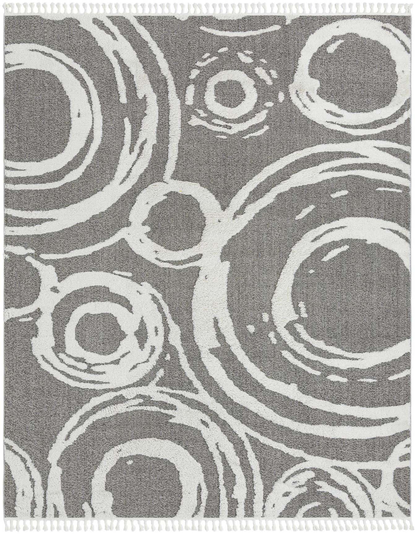A 10x14 rectangular gray area rug featuring a modern abstract pattern of large and small white concentric circles, with white tassels along the top and bottom edges.
