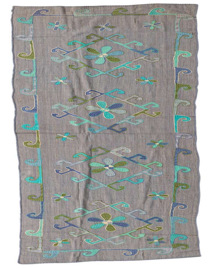 A 10 ft runner rug, the Kilim Suzani features a gray background with vibrant blue, green, and teal tribal floral patterns.