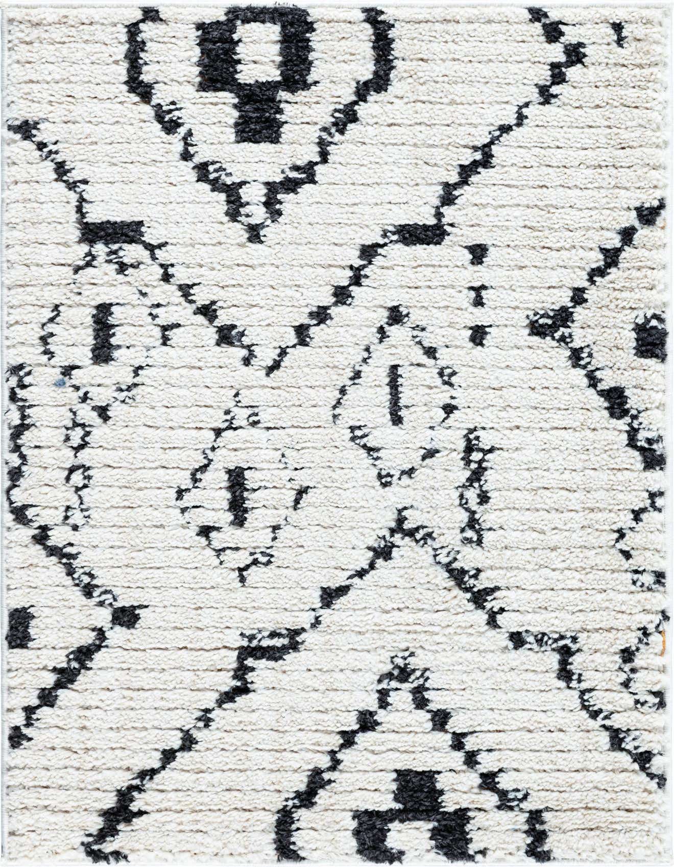 Close-up of a rectangular 2x3 ivory shag rug with a bold black abstract tribal pattern, showcasing its high, textured pile.