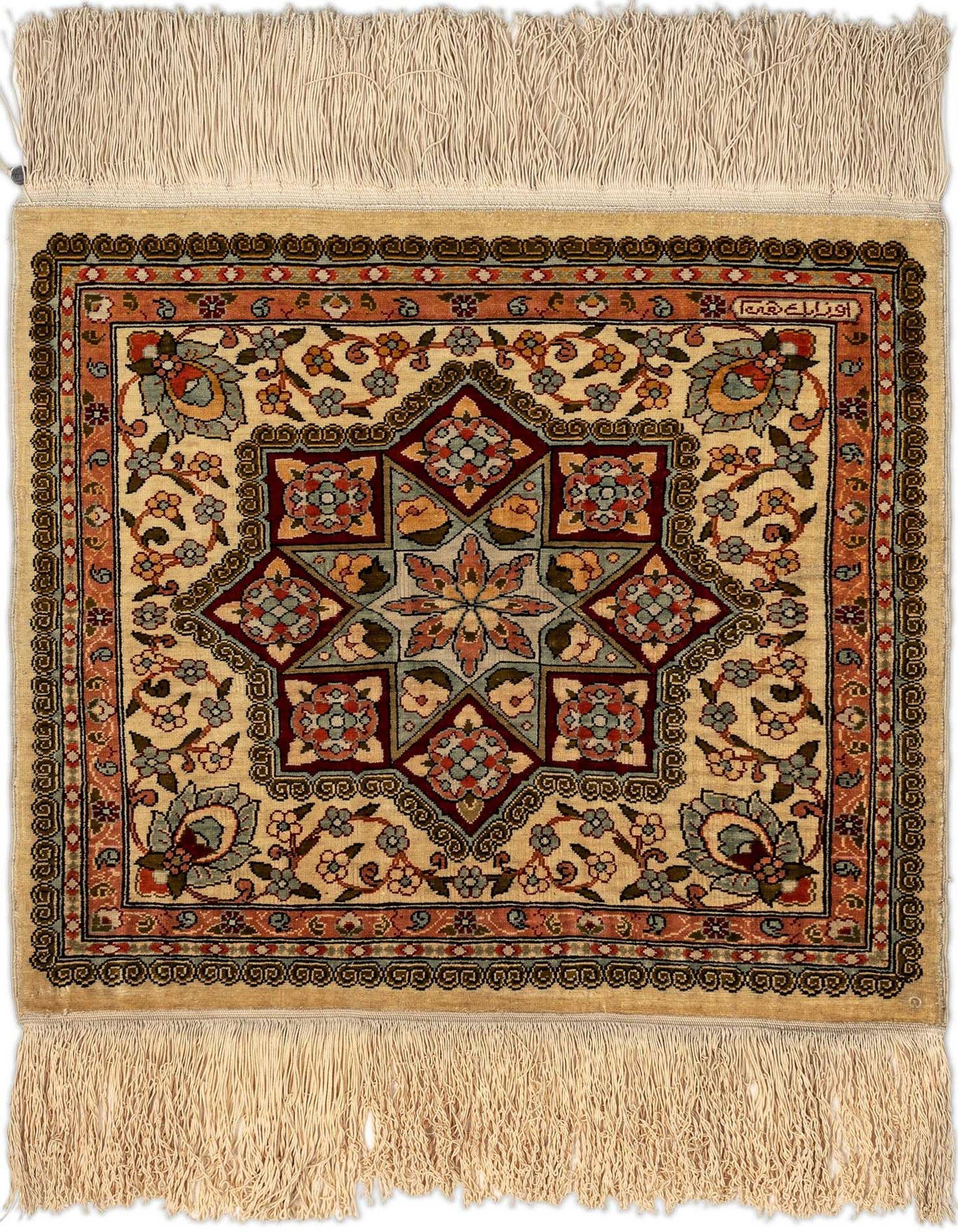 A small, square, multi-colored Persian silk rug with a central star medallion and floral motifs on a light background, featuring fringes.