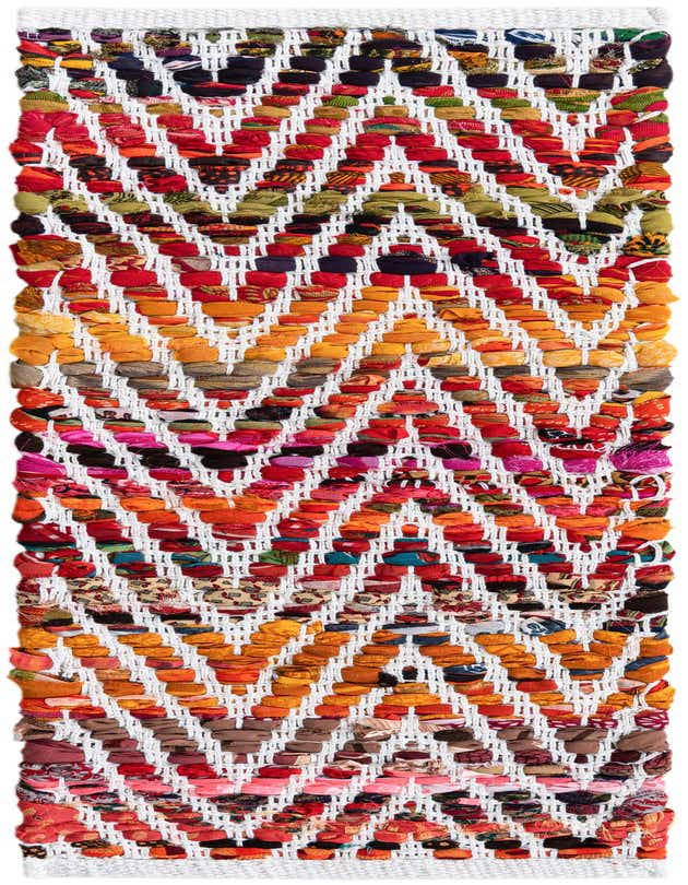 A close-up of a multi-colored Chindi Chevron stair rug, featuring a vibrant zigzag pattern made from woven recycled cotton fabric strips on a white base.