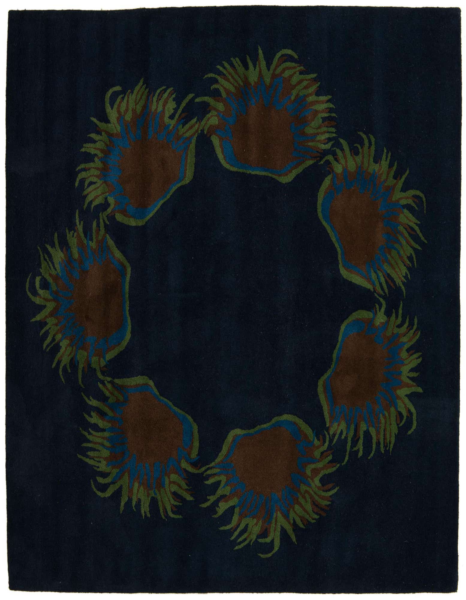 A square navy blue rug with a modern floral pattern of six brown, blue, and green abstract blossoms arranged in a circle.