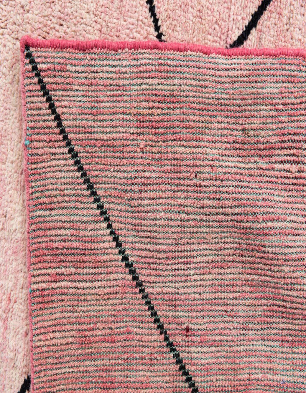 Close-up of a pink 5x8 rectangular shag rug with a black tribal pattern, showcasing its handmade wool texture.