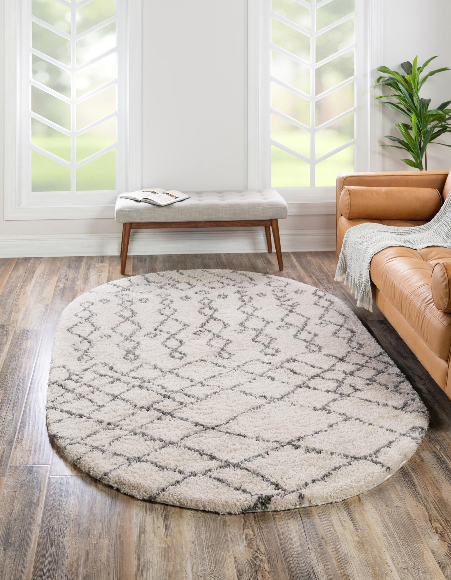 An oval ivory shag rug with a modern tribal trellis pattern in charcoal gray, suitable for an indoor living space.