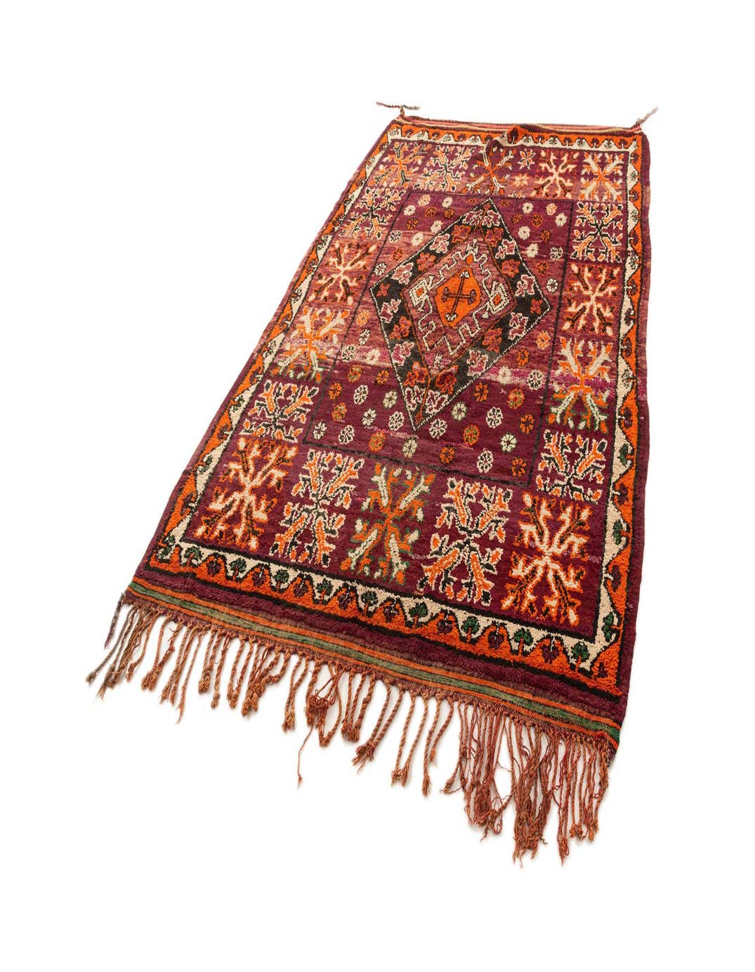 A 6x9 rectangular wool rug with a rich purple background and intricate orange, black, and cream geometric patterns, featuring tassels on the ends.