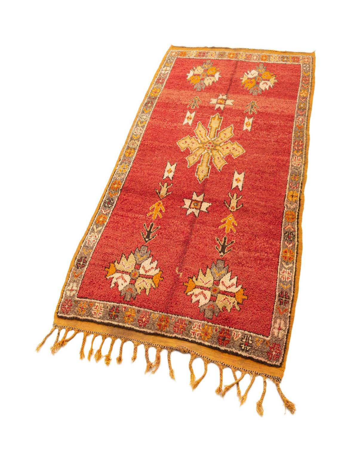 A 5x8 rectangular red wool rug with a vibrant geometric pattern in yellow, white, and gray, featuring a decorative border and fringes.