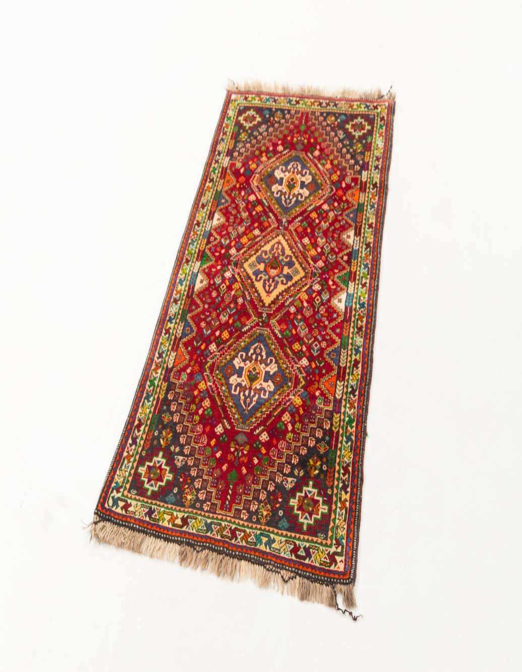 A 3x5 rectangular Ghashghai wool rug with a rich red background and intricate geometric patterns in blue, gold, and green.