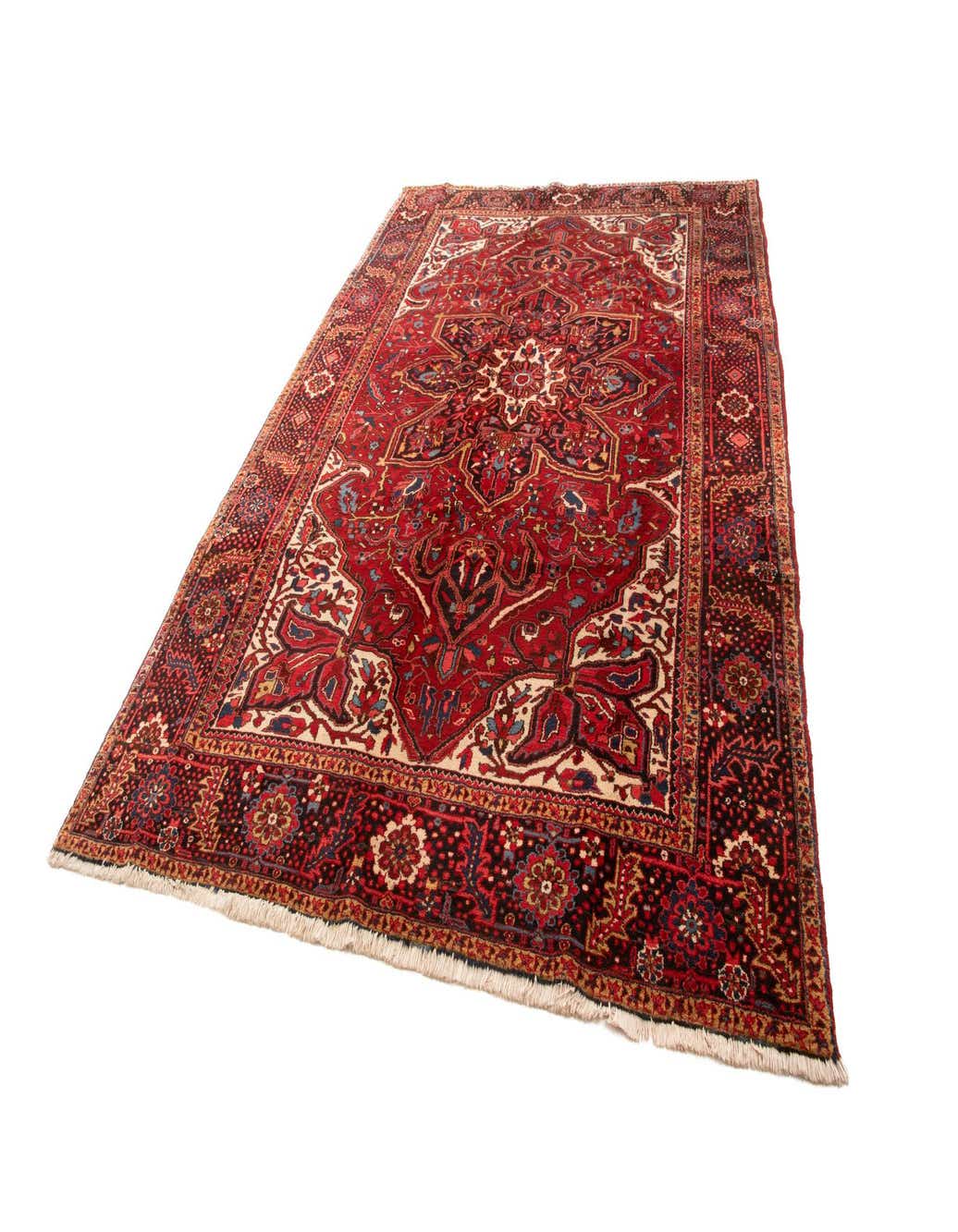A large 9x12 rectangular Heriz wool rug in rich reds with intricate traditional patterns and a detailed border.