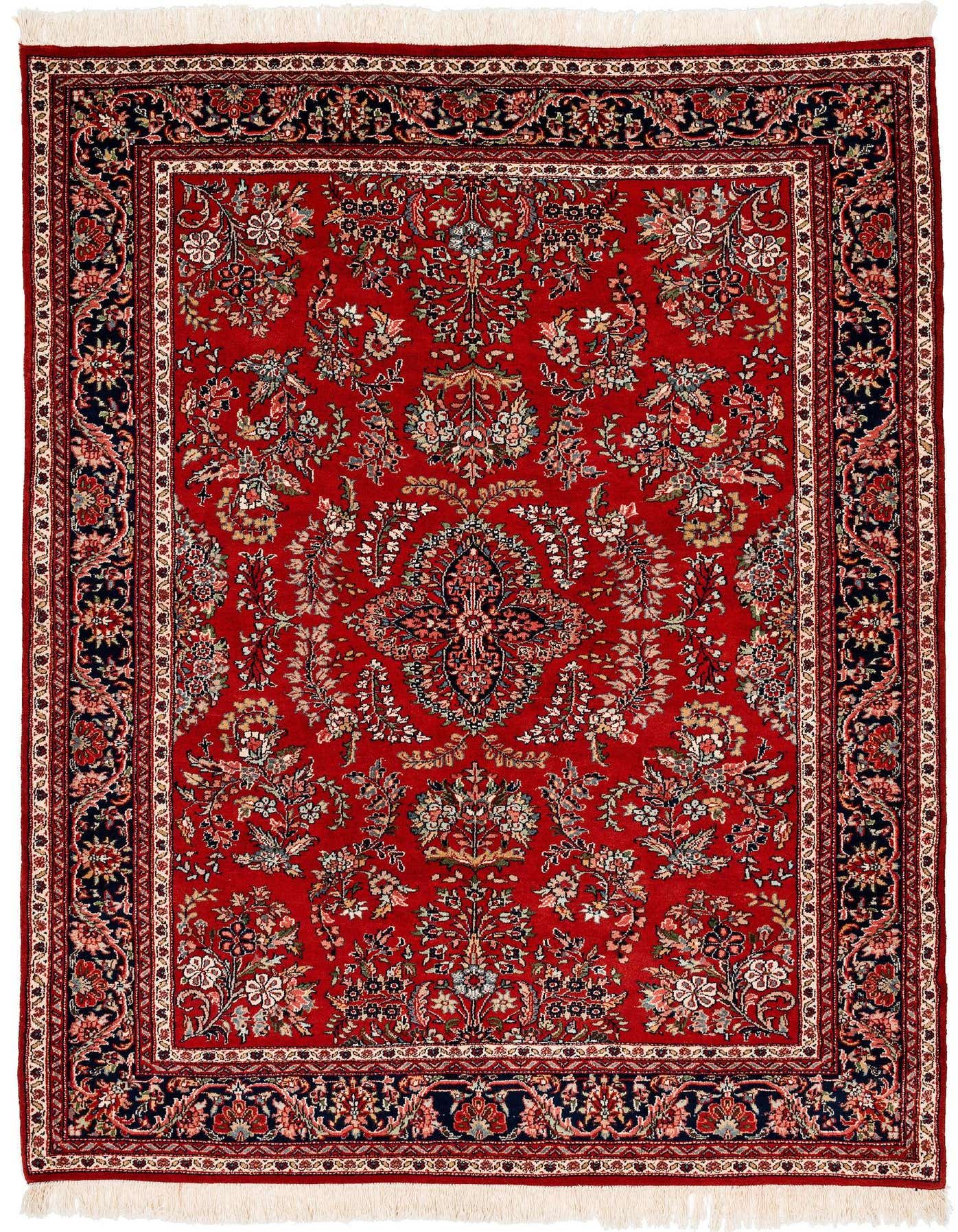 A 5x8 rectangular Sarouk area rug in deep red with intricate floral and medallion patterns, featuring a dark navy border and delicate fringes.