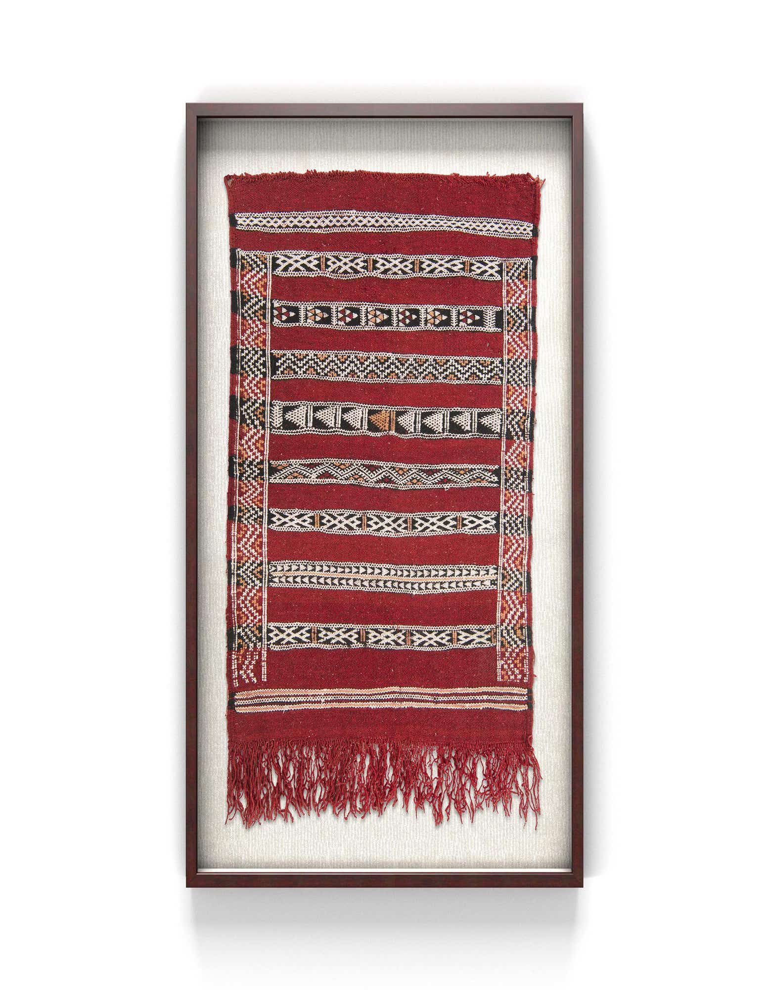 A framed 2x3 rectangular red textile wall art piece with horizontal stripes and geometric patterns in black, white, and tan.
