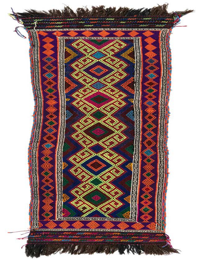 A vibrant 9 ft Kilim Fars runner rug with a bold geometric pattern in red, orange, purple, and green, featuring dark fringe.