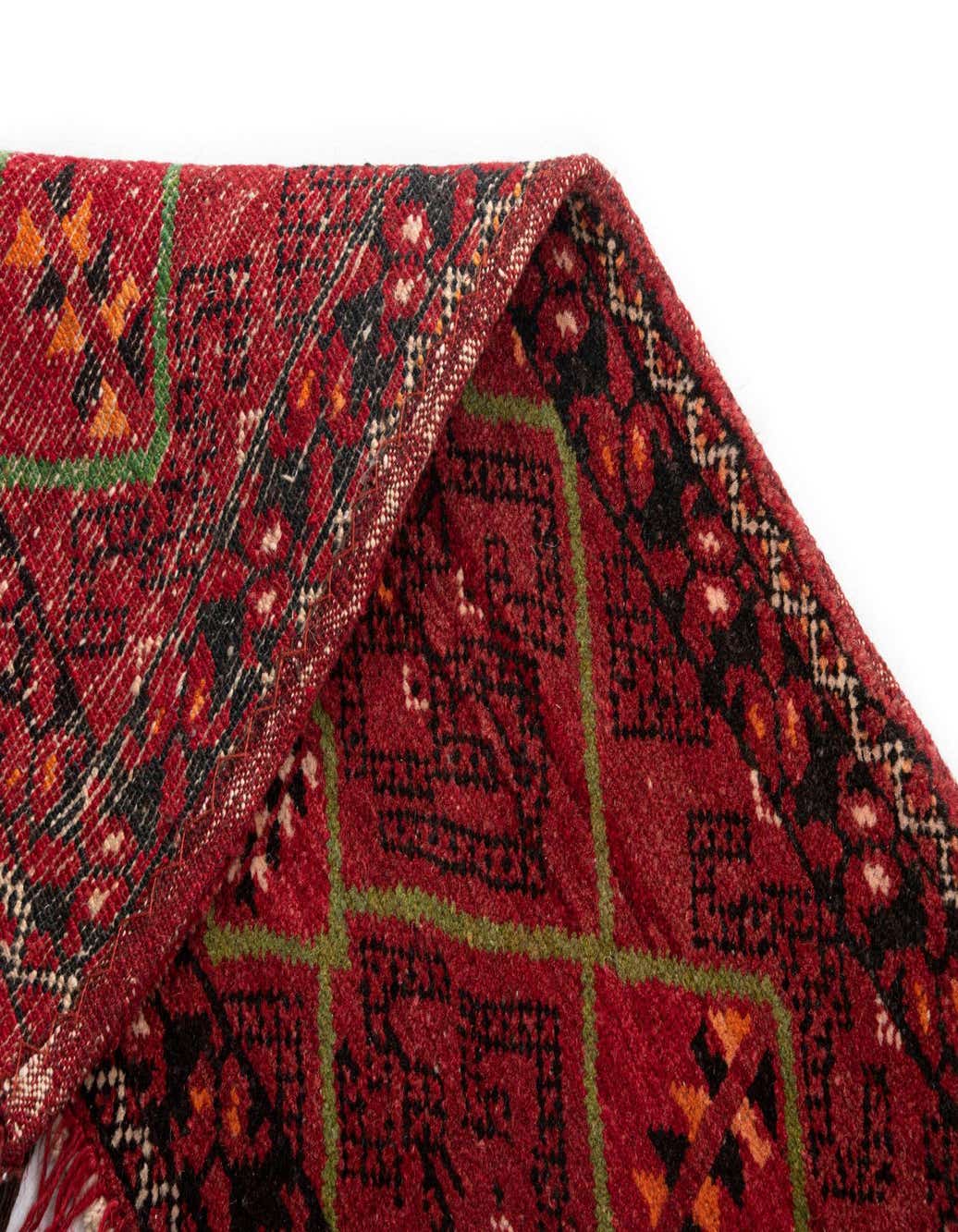 Close-up of a handmade 1' 4 x 5' 3 red wool Persian tribal runner rug with green and black geometric patterns.